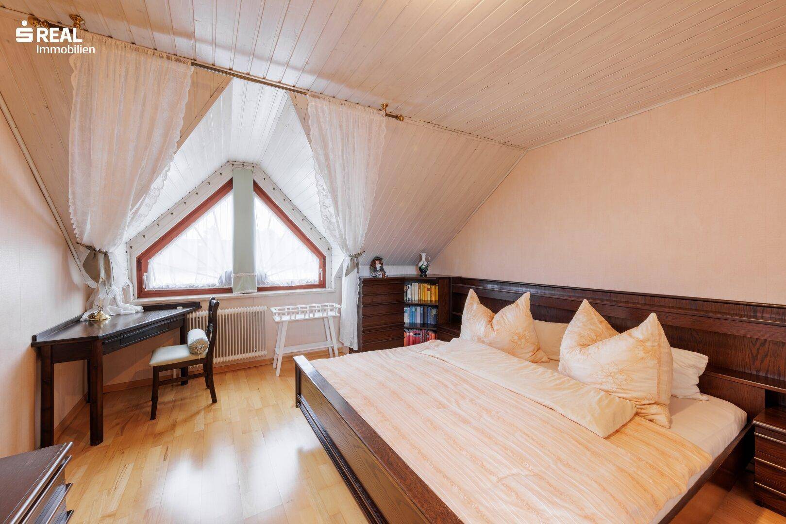 Schlafzimmer im Dachgeschoss mit Holzboden, Dachschrägen und einem großen Giebelfenster.