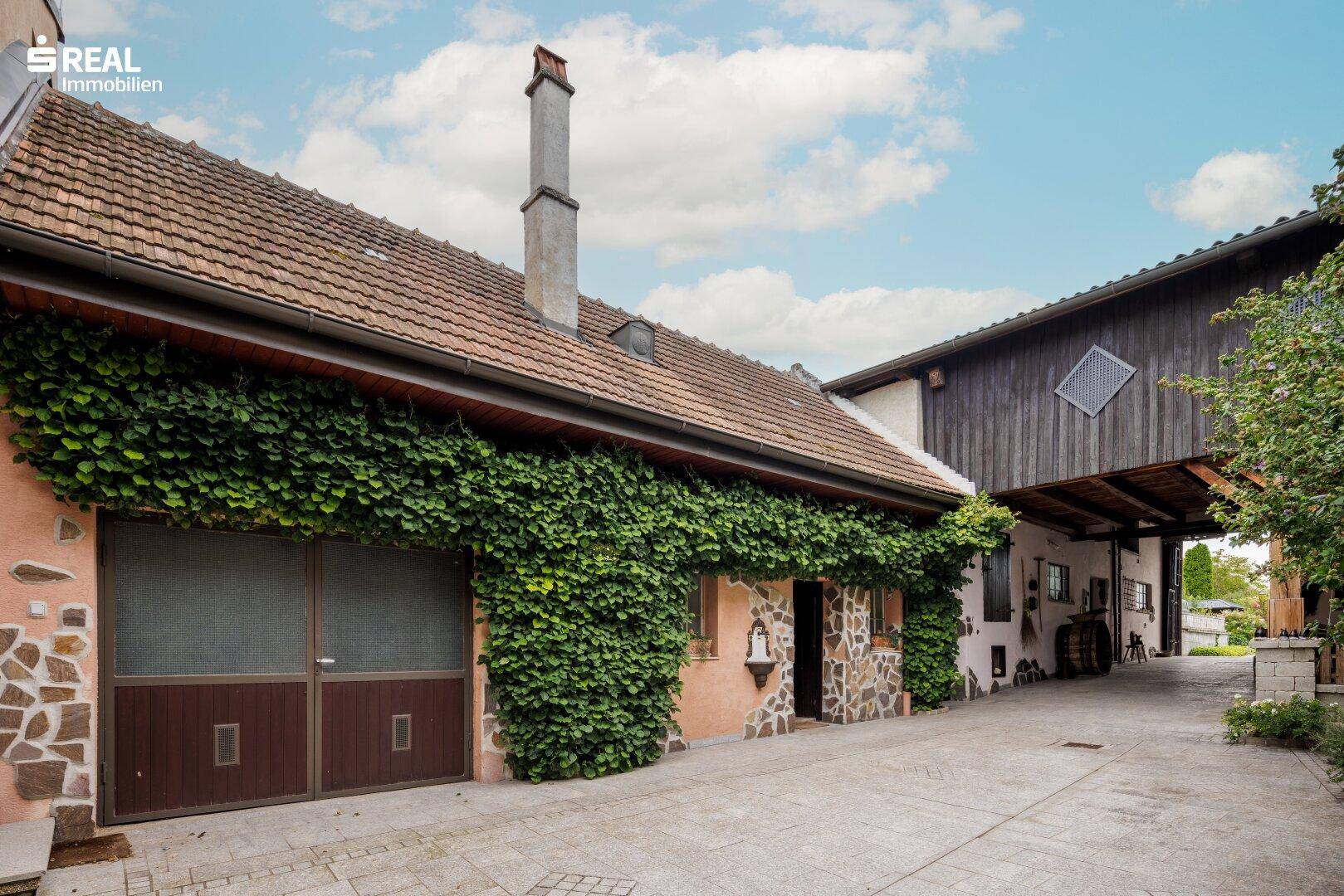 Traditionelle Fassade mit großen Garagentoren, bewachsenen Wänden und einem überdachten Eingangsbereich.