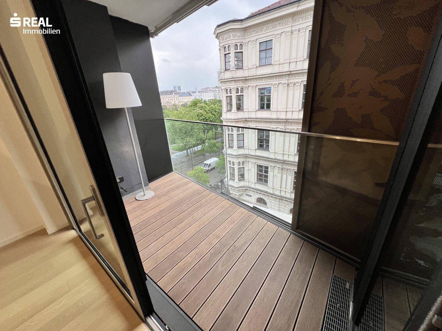 Balkon mit Holzboden und Glasgeländer bietet Blick auf die Stadt und historische Gebäude.
