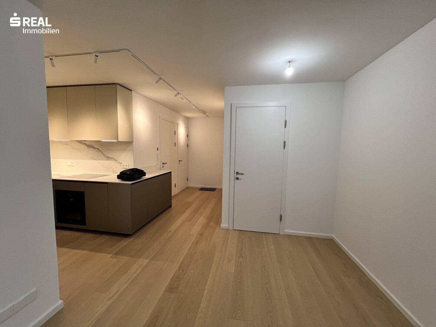Moderner Küchenbereich mit Holzboden und weißen Wänden in offenem Wohnraum.