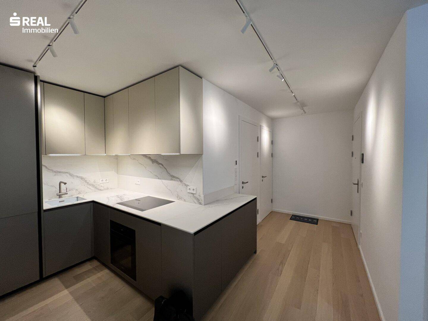 Elegante Einbauküche mit modernen Geräten, weißen Arbeitsplatten und Holzboden.