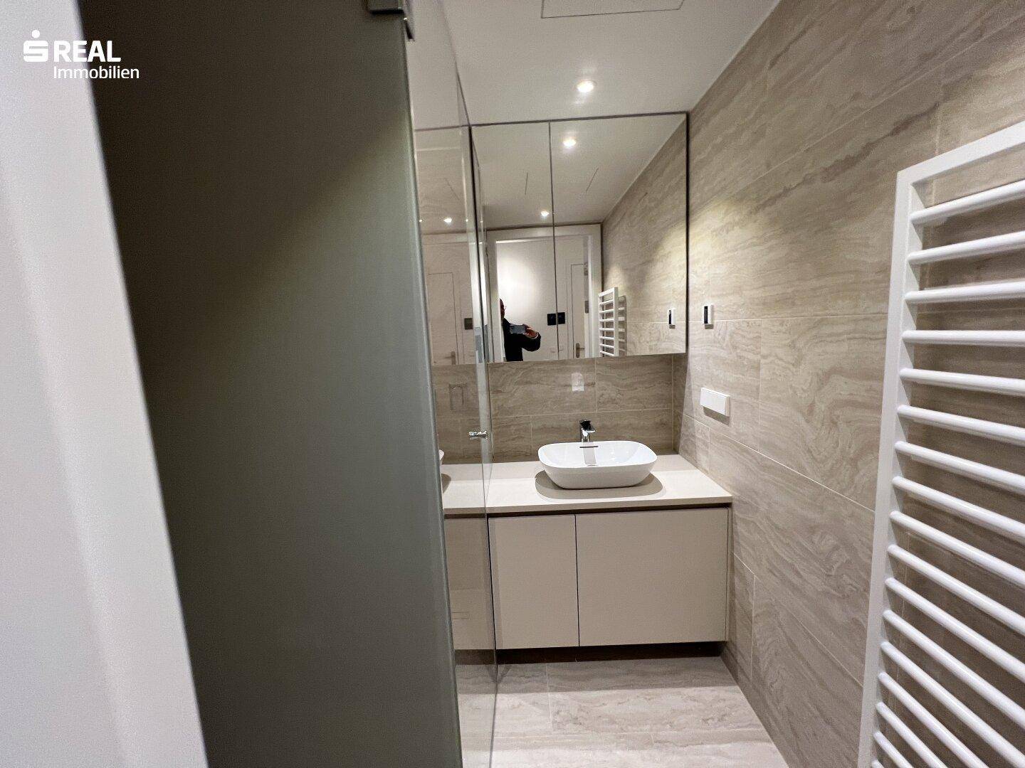 Modernes Badezimmer mit eleganten Fliesen, Einzelwaschbecken und beheiztem Handtuchhalter.