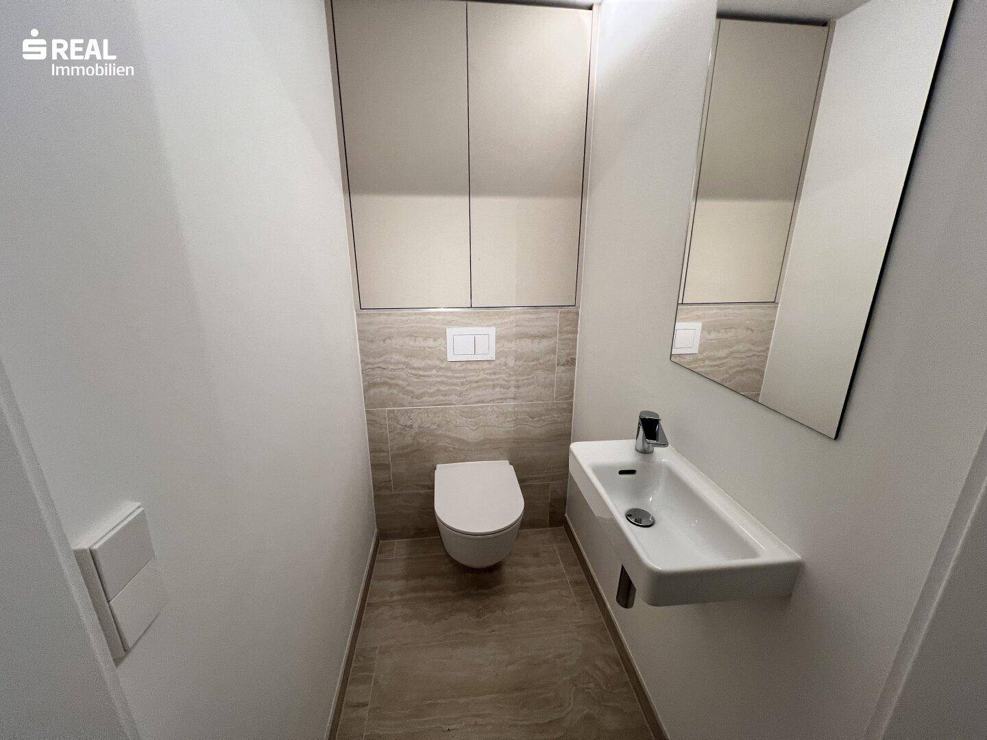 Gäste-WC mit wandhängender Toilette, kleinem Waschbecken und modernen Fliesen.