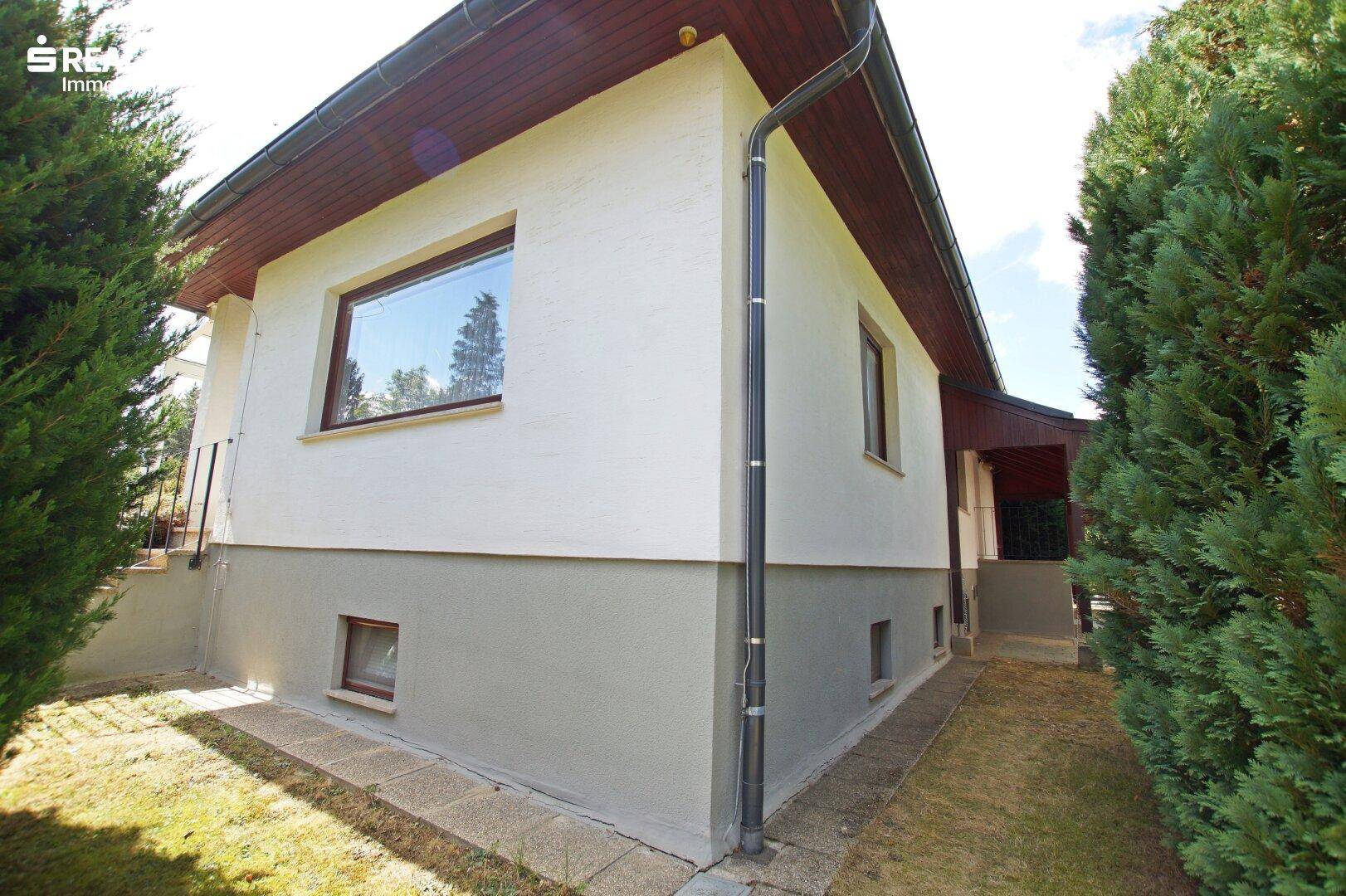 Seitenansicht des Hauses mit weißer Fassade, kleinen Fenstern und Dachüberstand.