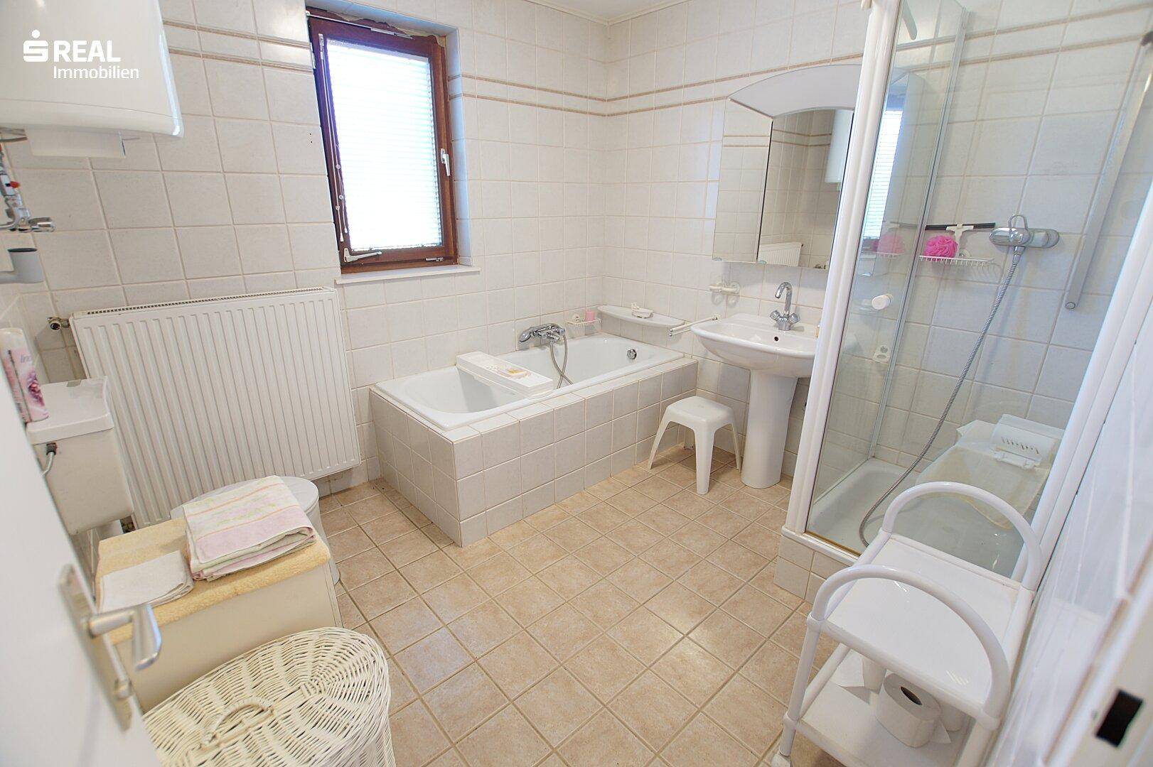 Helles Badezimmer mit Badewanne, Duschkabine, WC und Fenster.