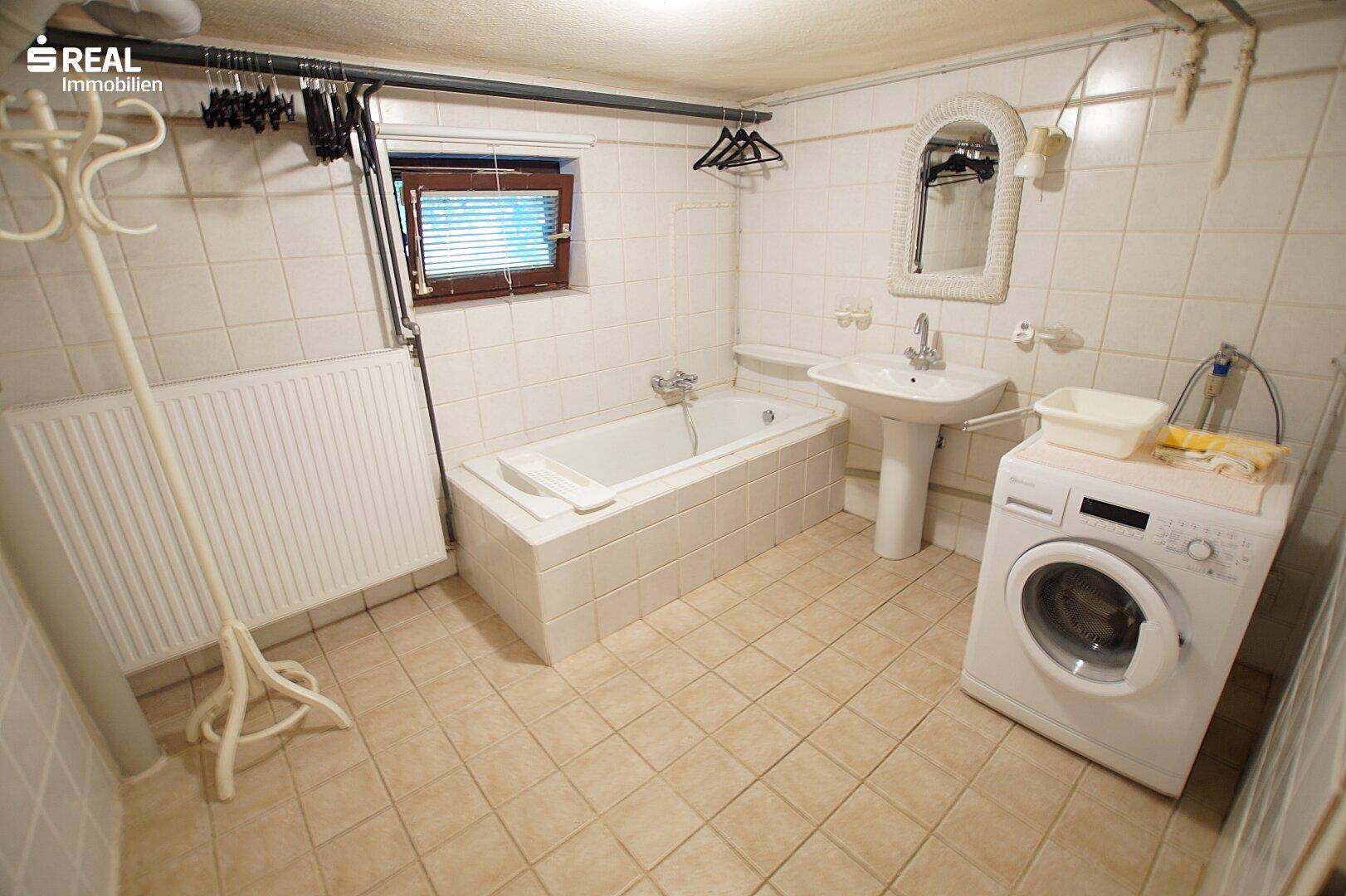 Badezimmer im Keller mit Waschmaschine, Badewanne und Fliesenboden.