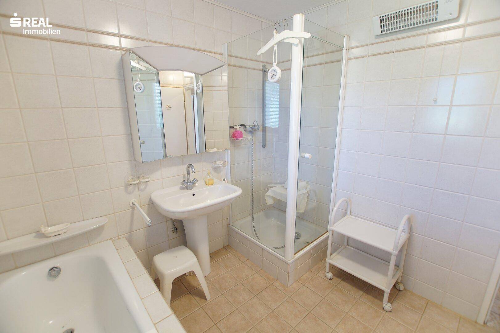 Badezimmer mit Duschkabine, Waschtisch und Spiegelschrank, praktisch eingerichtet.