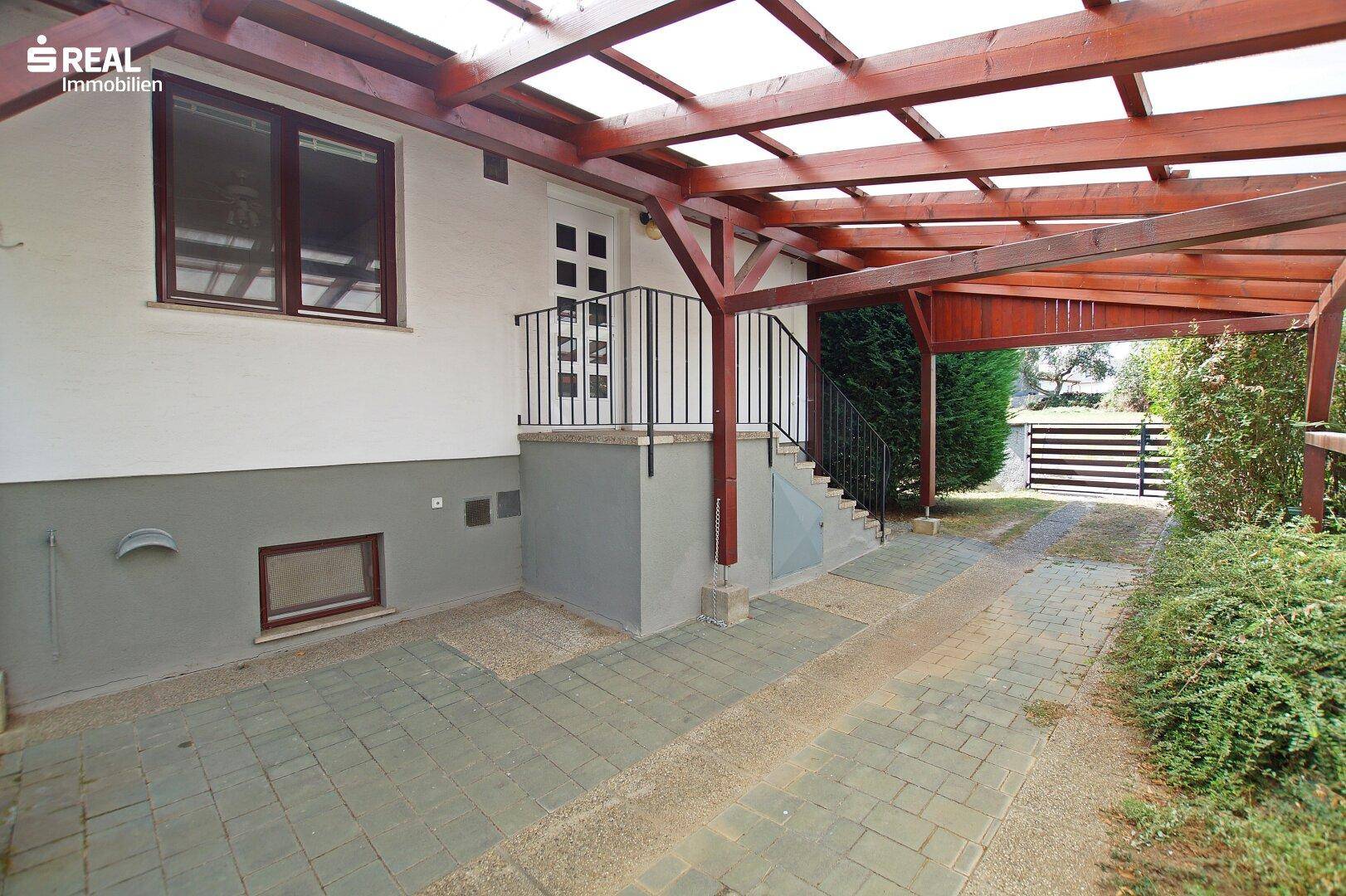 Carport und Eingangsbereich mit gepflasterter Zufahrt und Blick auf das Gartentor.