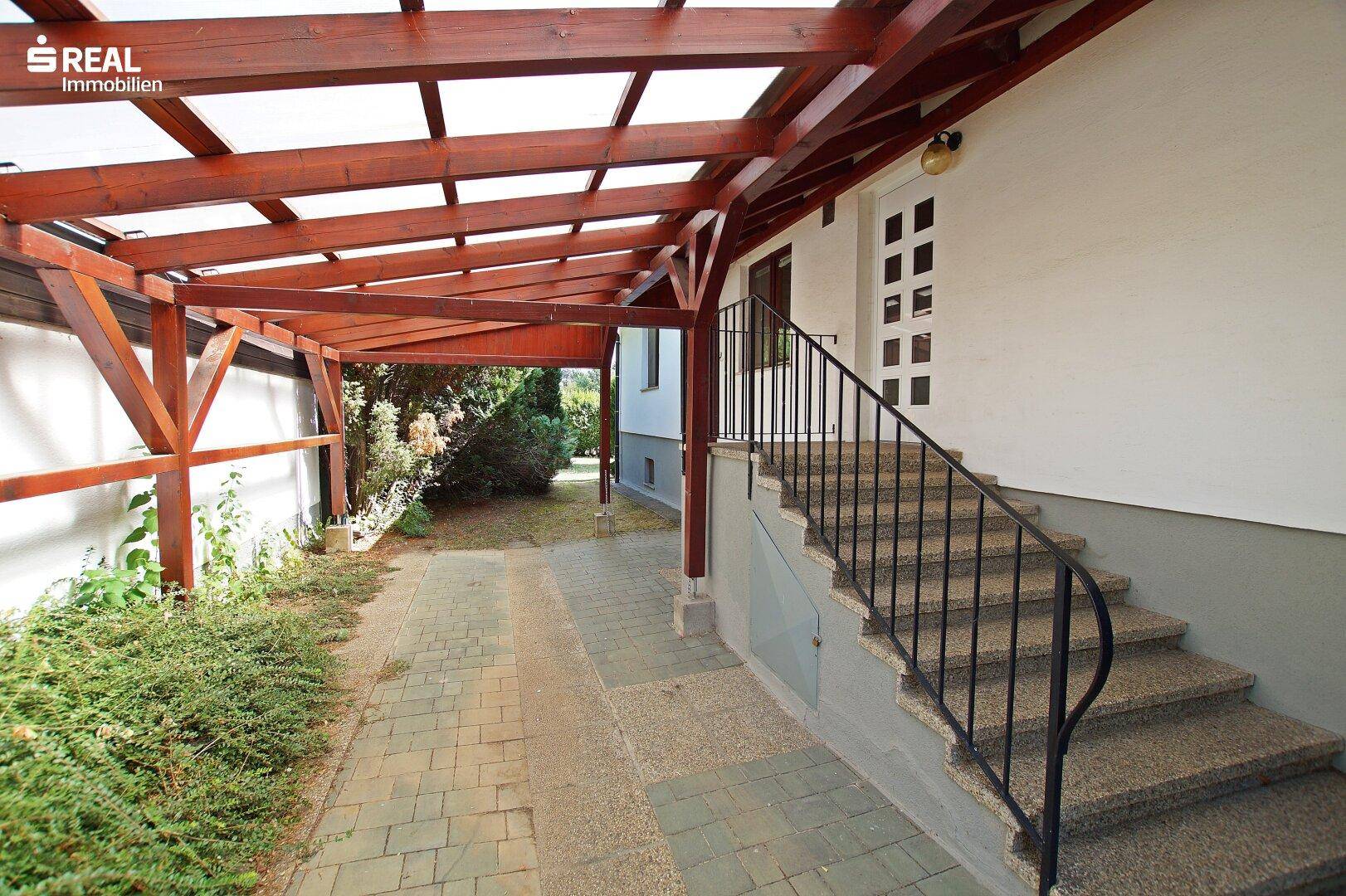Überdachter Eingangsbereich mit Holzcarport und Außentreppe zum Hauszugang.