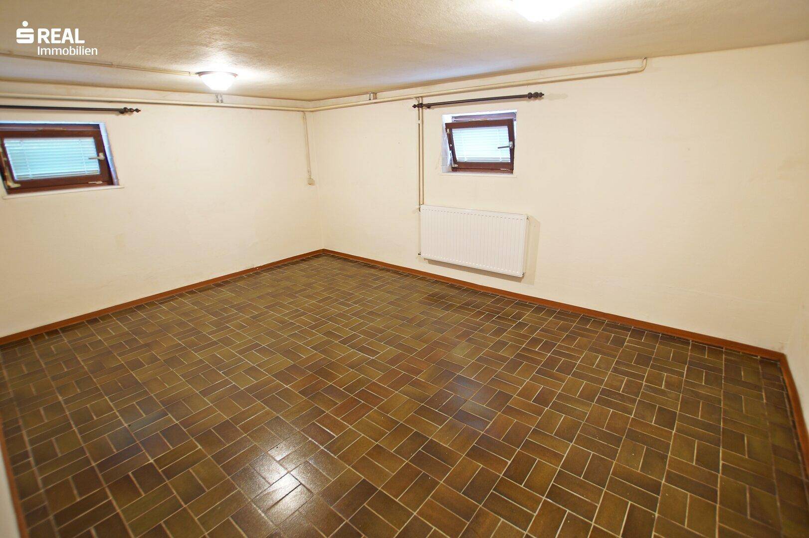 Geräumiger Kellerraum mit Fliesenboden und kleinen Fenstern für Tageslicht.