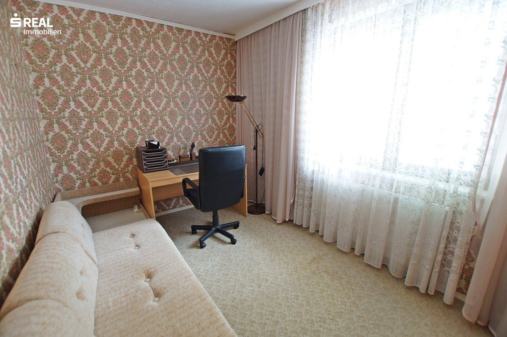Helles Arbeitszimmer mit Schreibtisch, Sofa und Teppichboden, ideal für Home-Office.