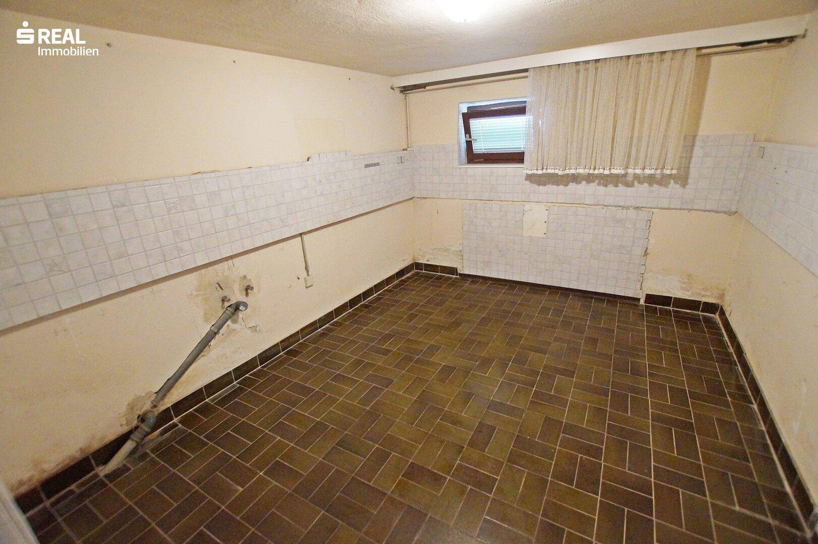 Kellerraum mit Fliesenboden und teilweiser Wandverkleidung, renovierungsbedürftig.