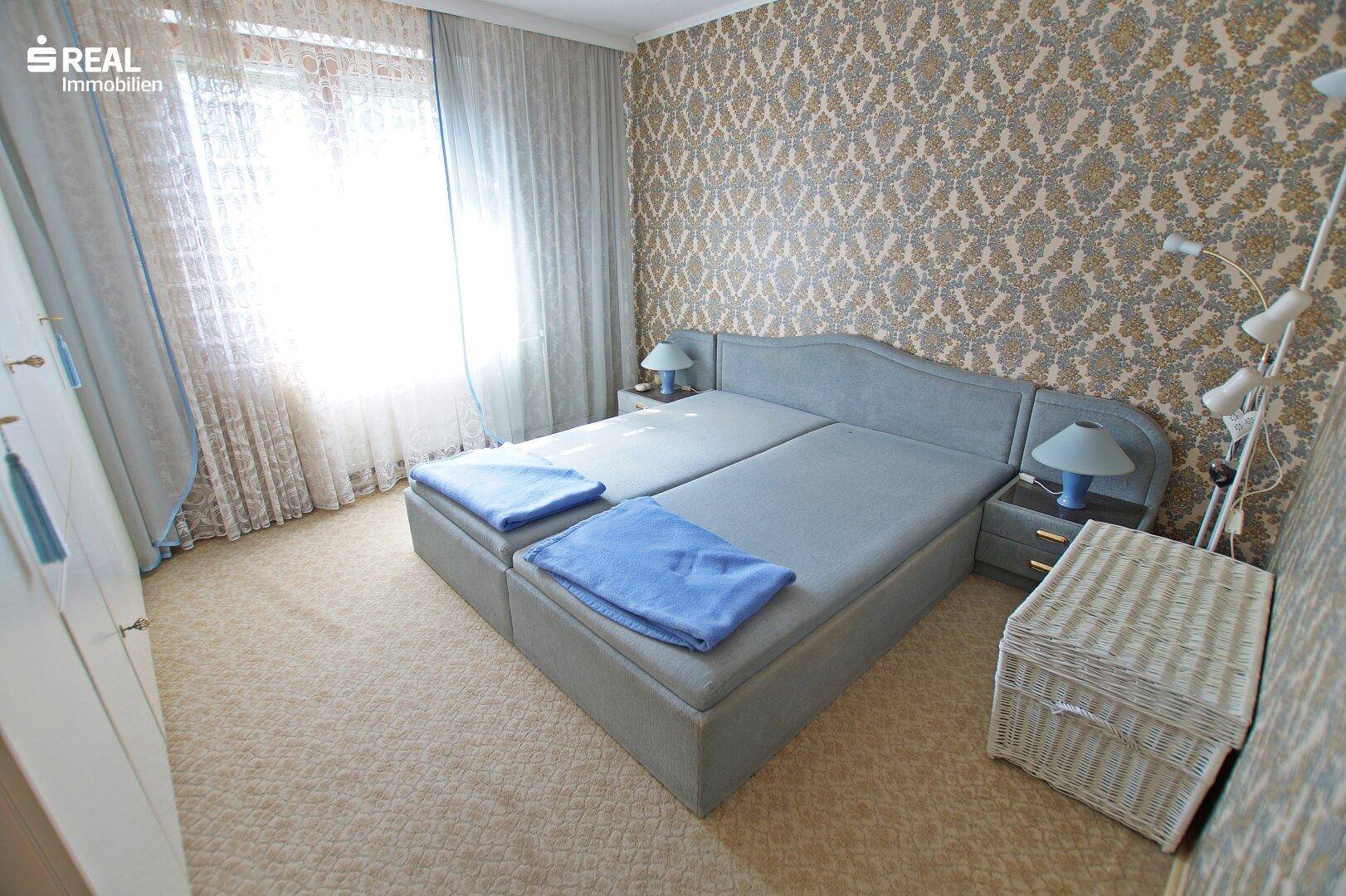 Weiteres Schlafzimmer mit gemusterter Tapete, Teppichboden und Doppelbett.