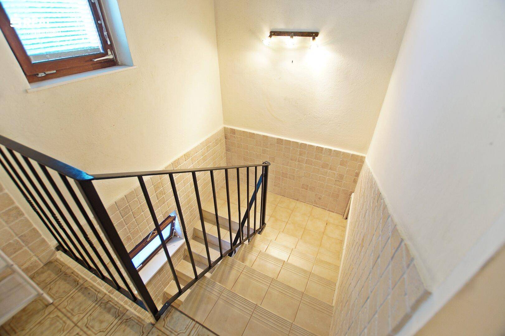 Treppenhaus mit Fliesen und Geländer, das zum Kellergeschoss führt.