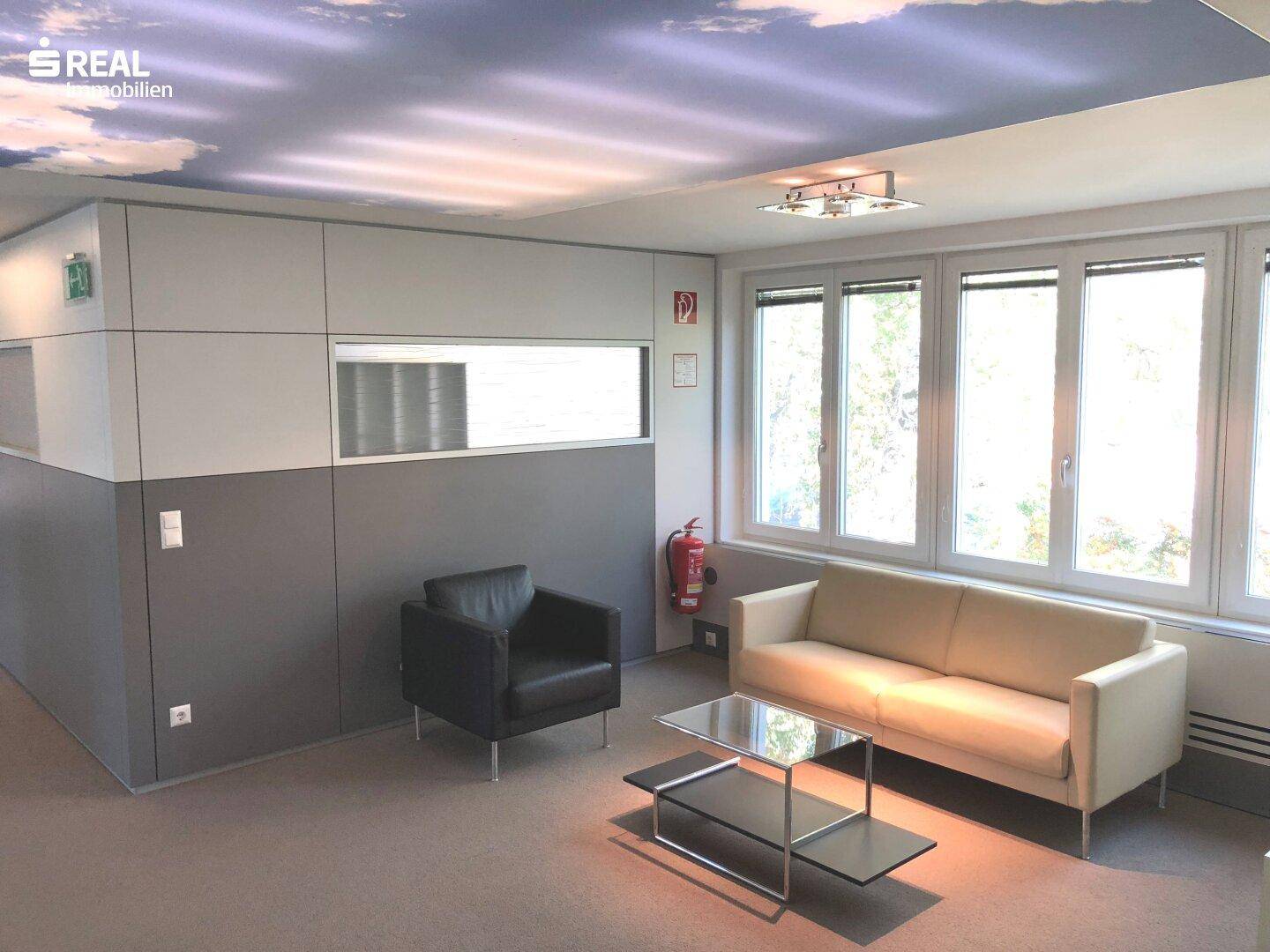 Gemütlicher Wartebereich im Büro mit bequemen Sofas, einem Couchtisch und großen Fenstern.