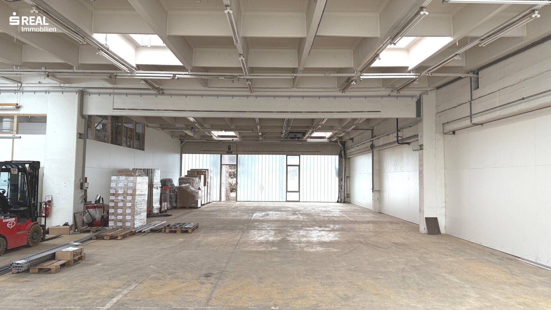 Helle Lagerhalle mit Oberlichtern, Betonboden und einem Gabelstapler im Hintergrund.