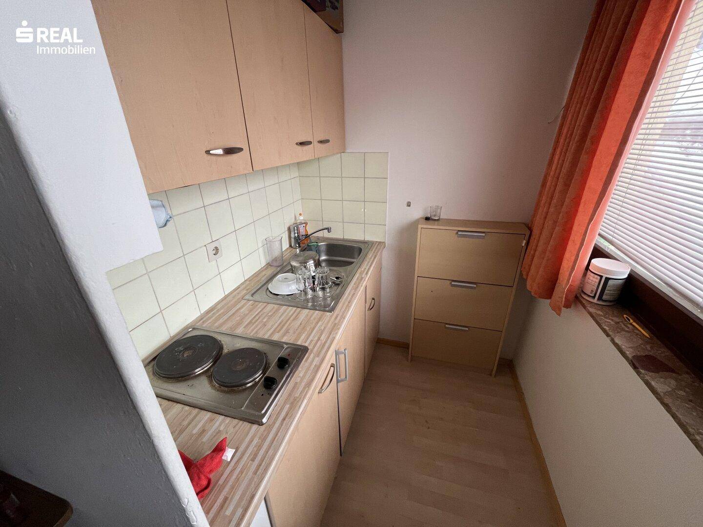 Kleine Küchenzeile mit zwei Kochplatten, Spüle und Oberschränken in hellem Holzdekor.