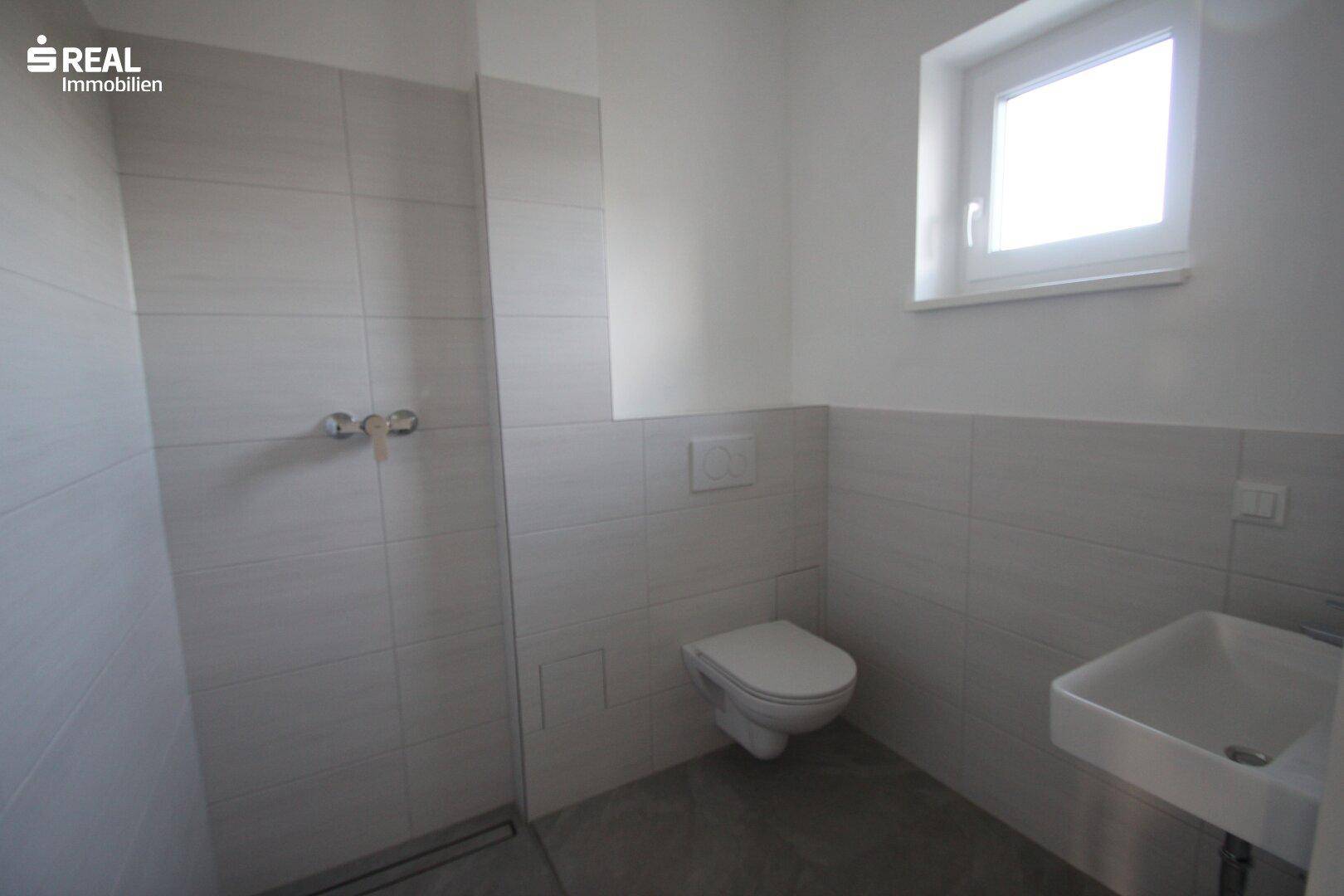 Modernes Badezimmer mit Dusche, wandhängendem WC, Waschbecken und einem Fenster für Tageslicht.