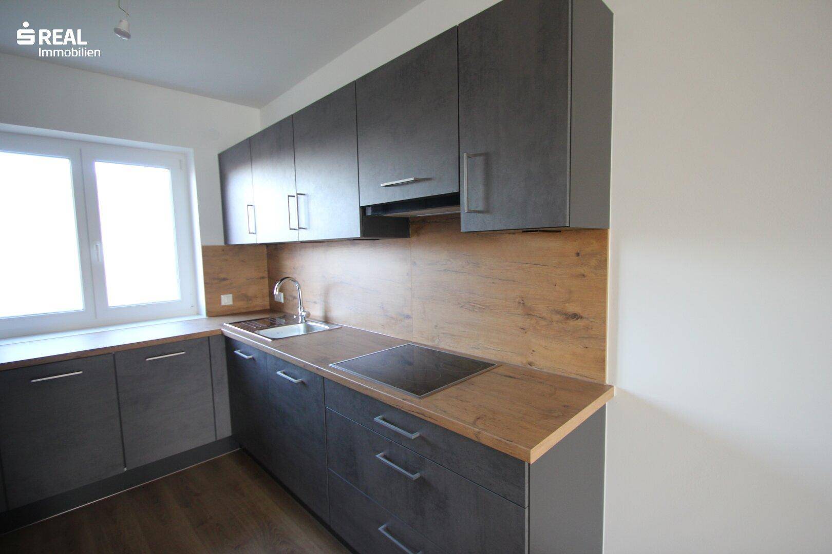 Detailansicht der modernen Küche mit Spüle, Induktionskochfeld und Holzoptik-Rückwand.