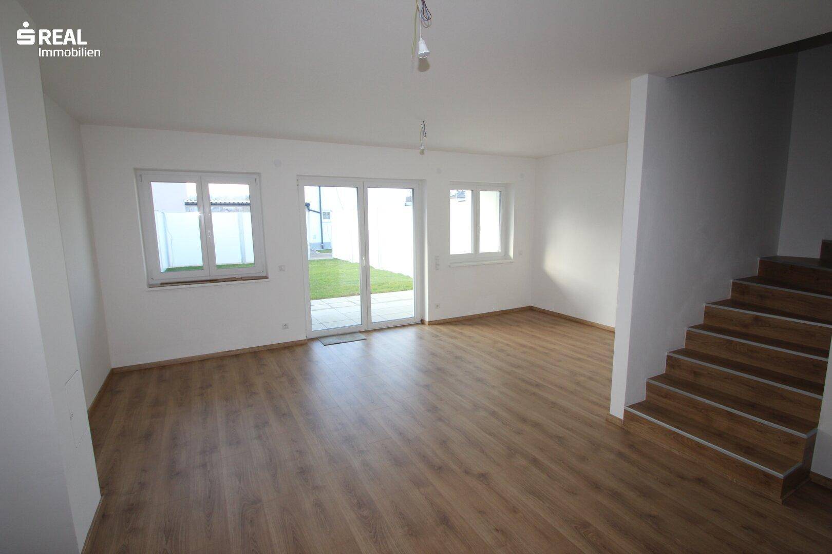 Helles Wohnzimmer mit Laminatboden, weiß gestrichenen Wänden und Zugang zum Garten.