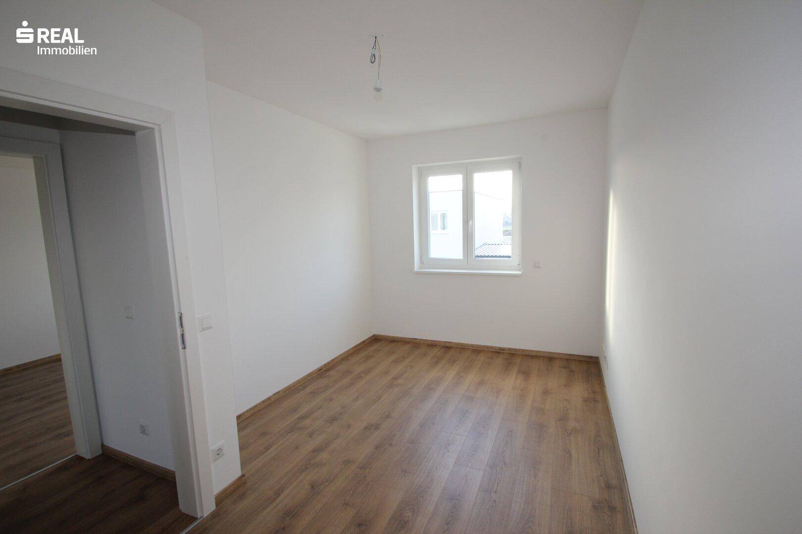Helles Schlafzimmer mit Laminatboden, weißen Wänden und einem großen Fenster für viel Licht.