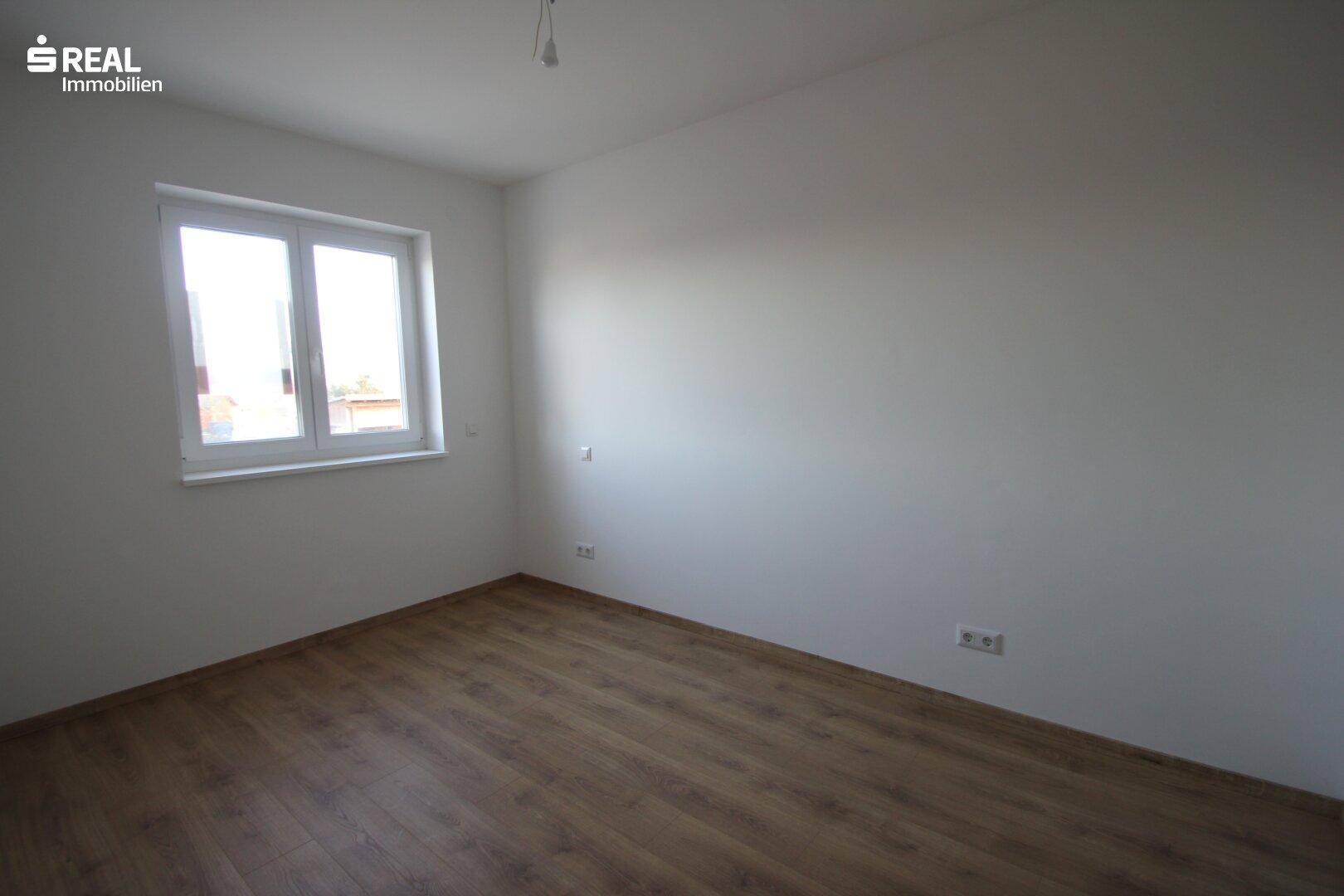 Einfaches Schlafzimmer mit Laminatboden und Fenster, das viel natürliches Licht hereinlässt.