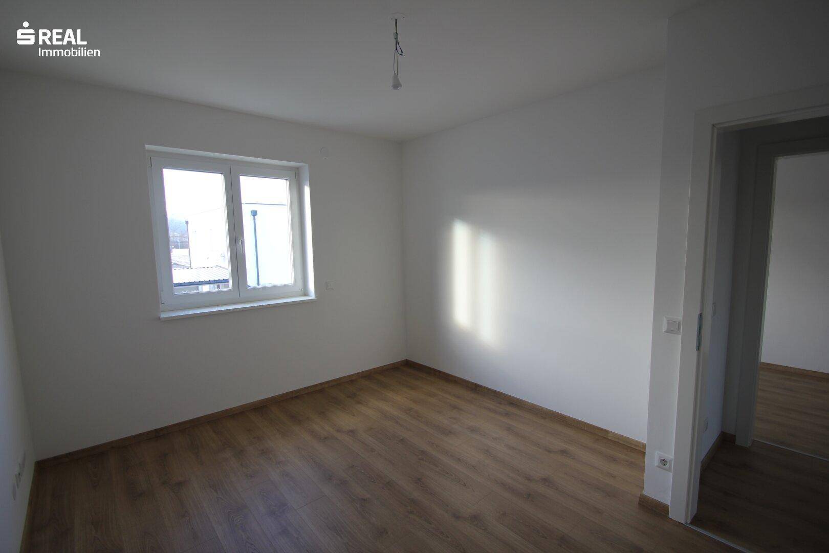 Geräumiges Schlafzimmer mit Laminatboden und Fenster, das viel Tageslicht hereinlässt.