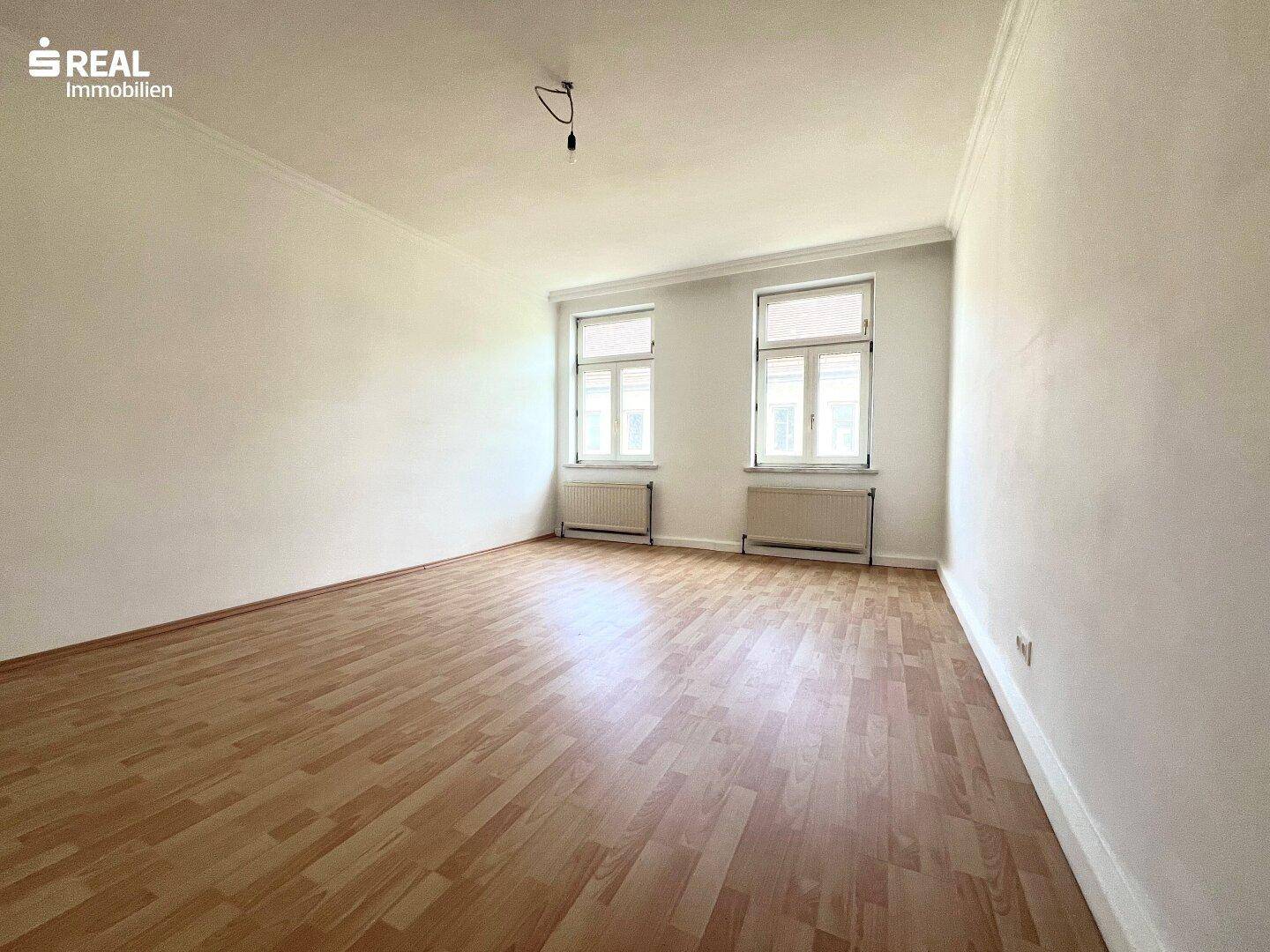 Geräumiger, heller Wohnraum mit Laminatboden und großen Fenstern für viel Tageslicht.