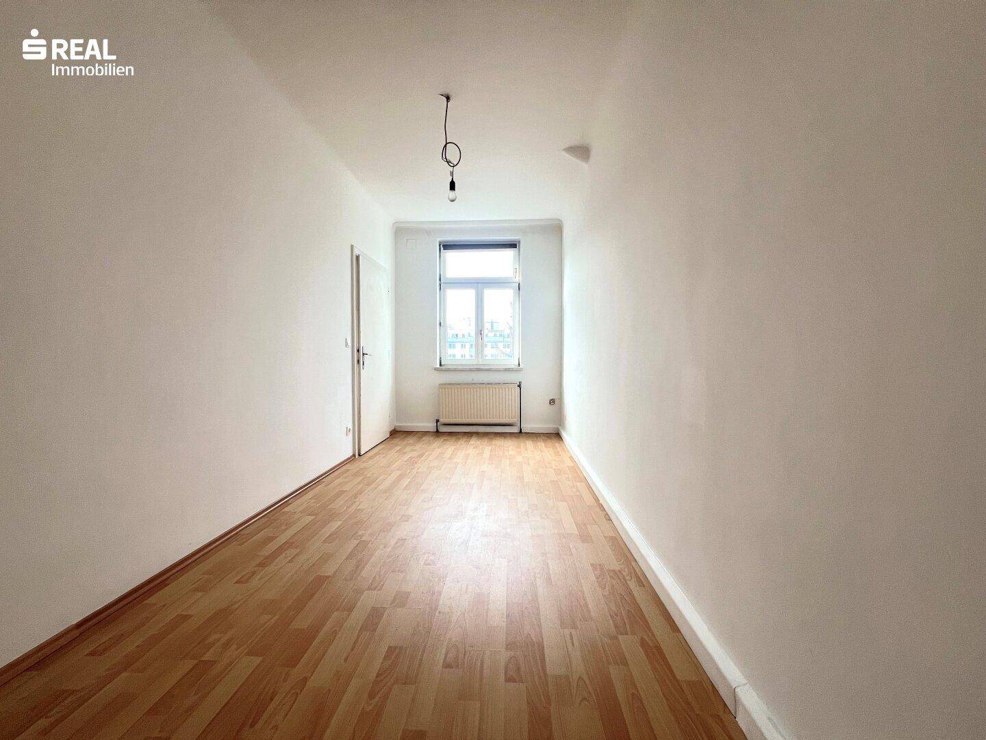 Helles Zimmer mit Laminatboden, einem Fenster und weiß gestrichenen Wänden.