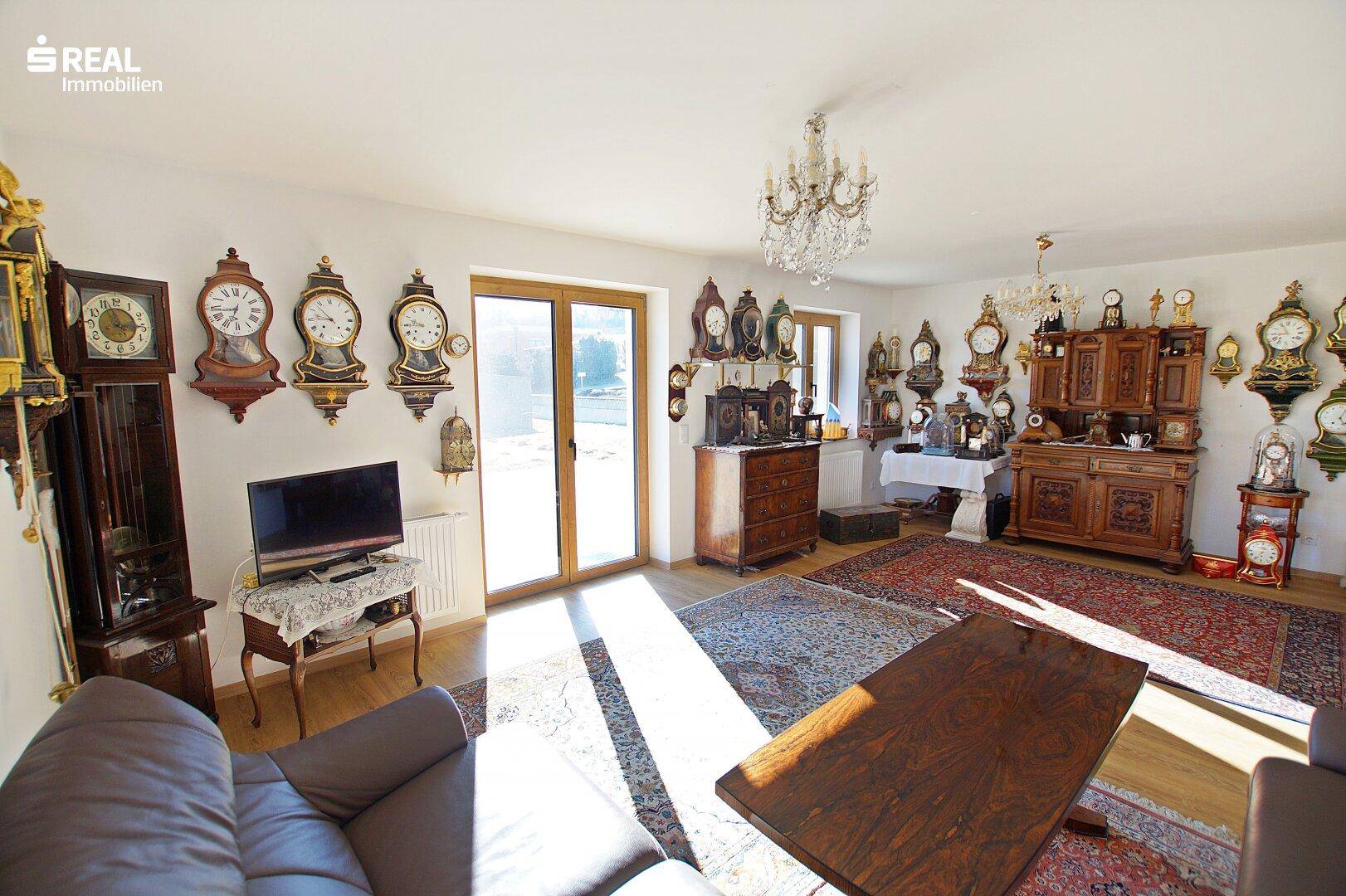 Gemütliches Wohnzimmer mit dunklen Holzmöbeln, Teppichen und viel Tageslicht.
