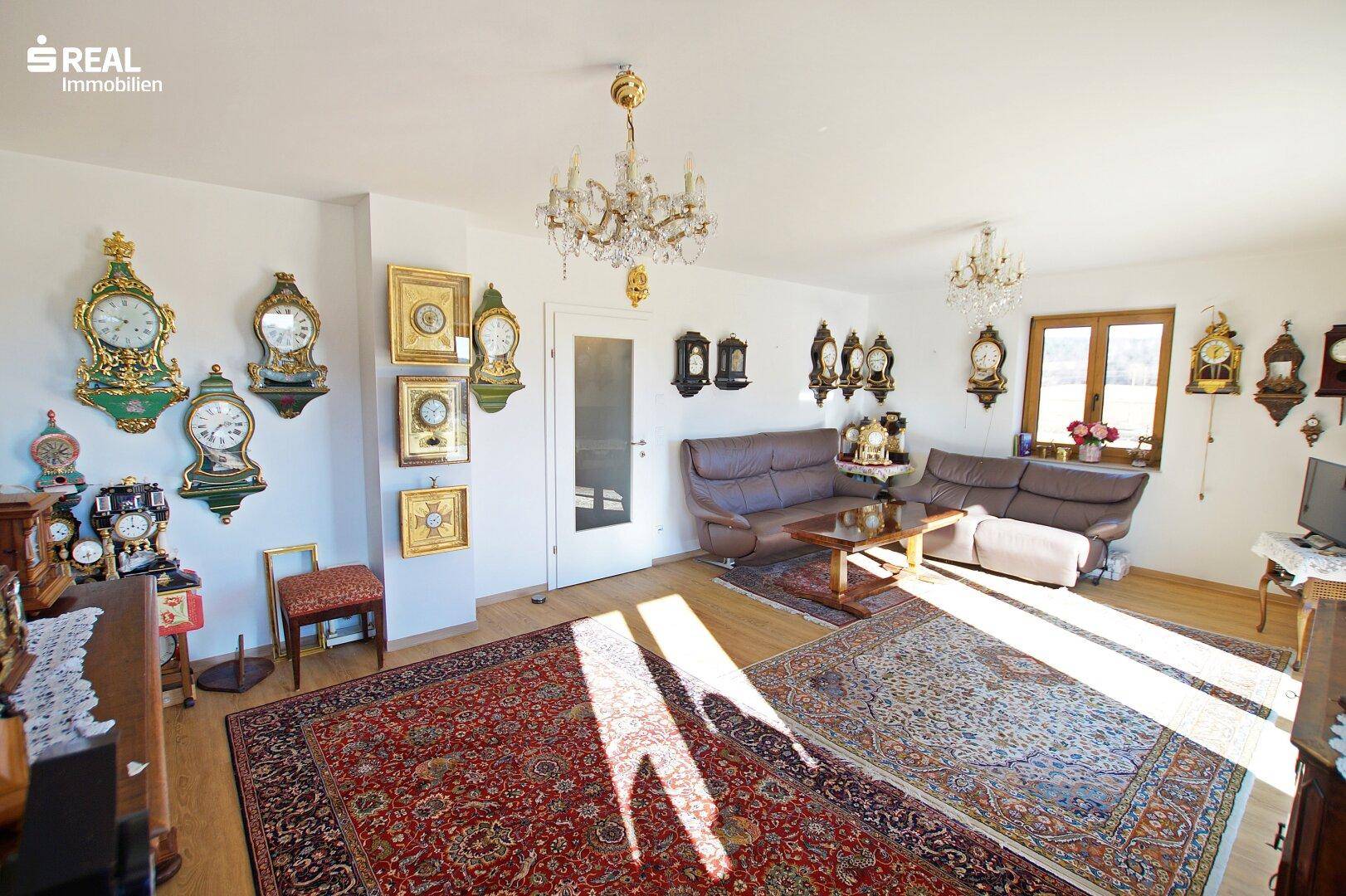 Helles Wohnzimmer mit bequemen Sofas, Kronleuchter und einer Sammlung antiker Uhren.