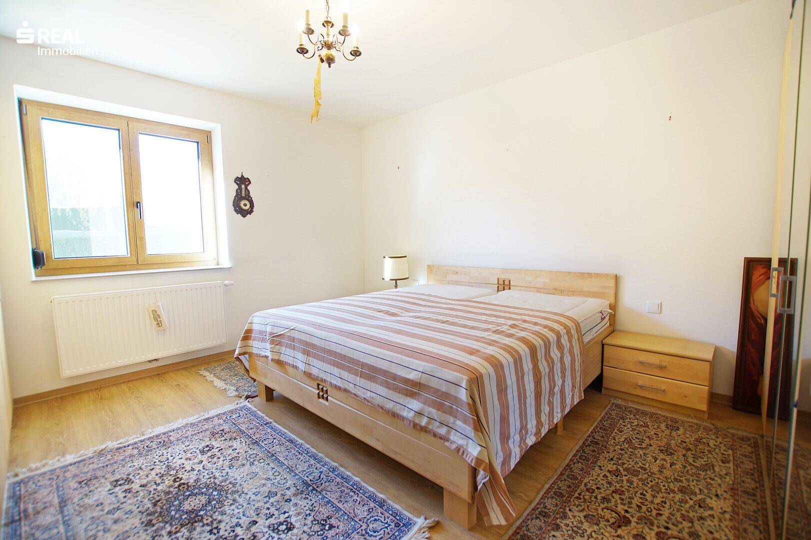 Helles Schlafzimmer mit Holzbett, Teppichen und großem Fenster.