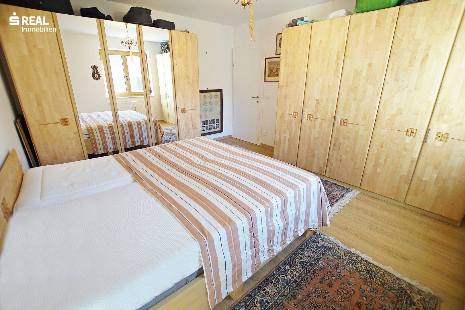 Schlafzimmer mit Holzboden, Einbauschränken und einem großen Spiegel.