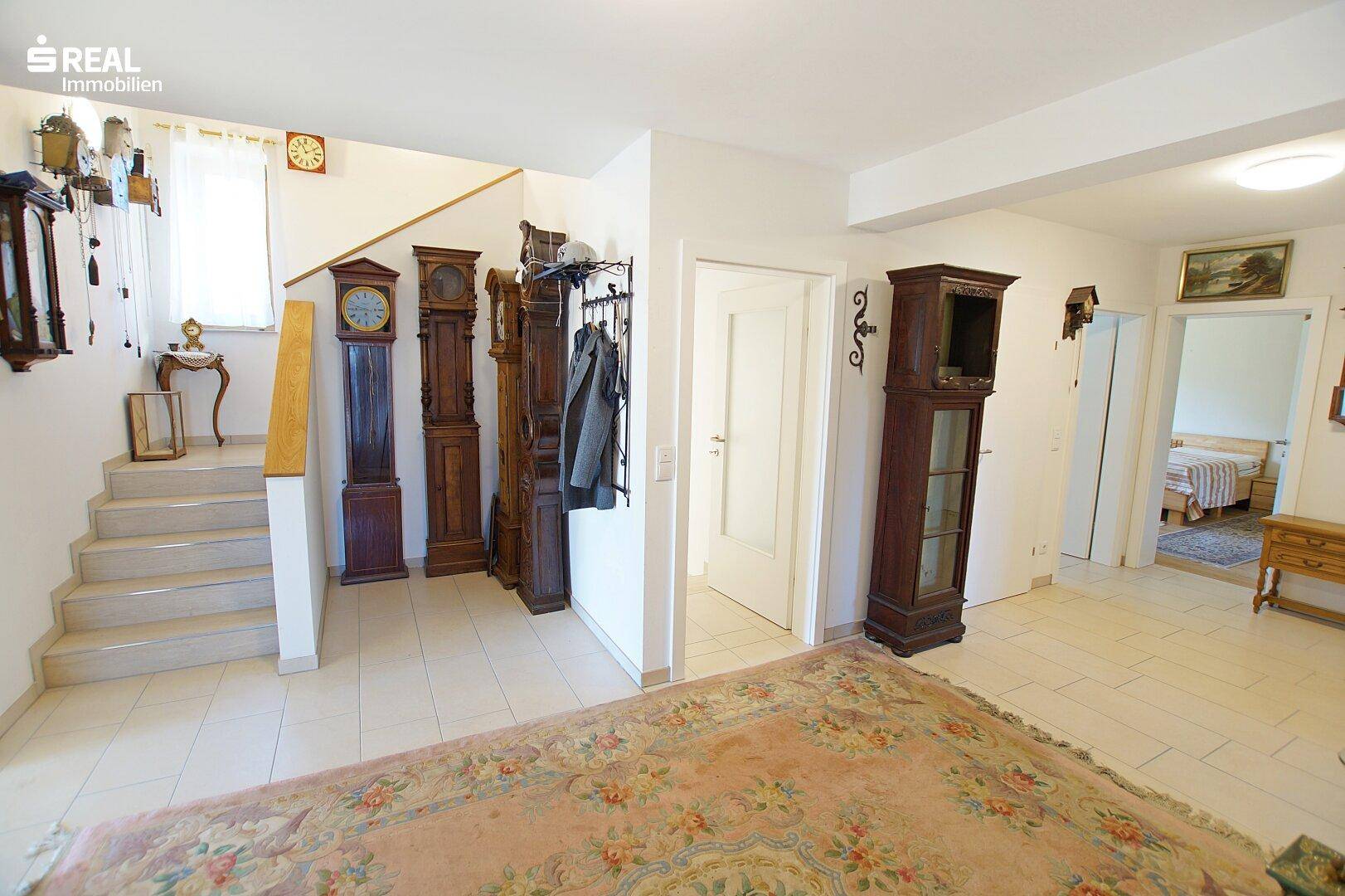 Heller Eingangsbereich mit Treppe, Fliesenboden und traditionellen Standuhren.