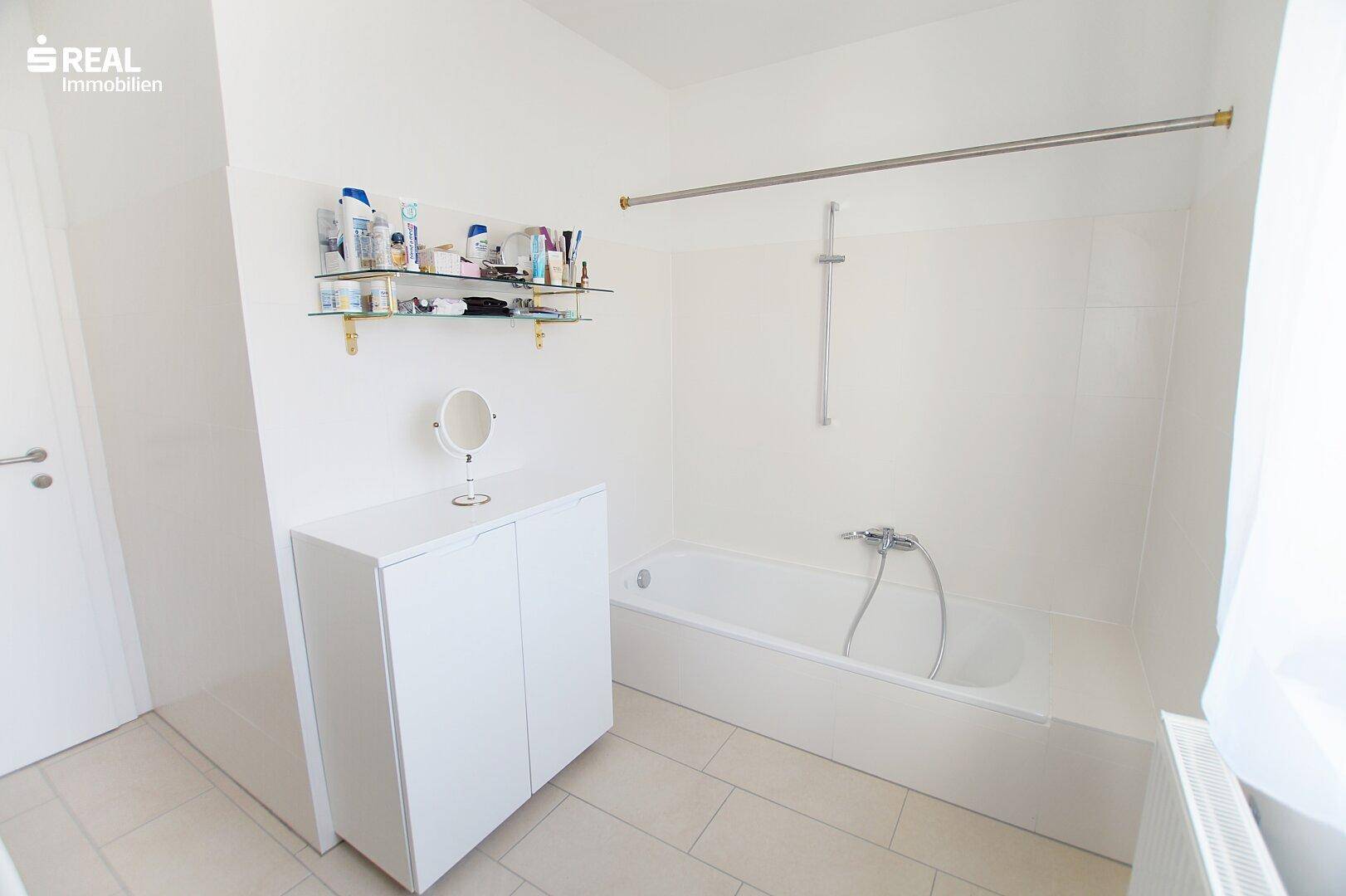 Weißes Badezimmer mit Badewanne, Fliesenboden und einfacher Einrichtung.
