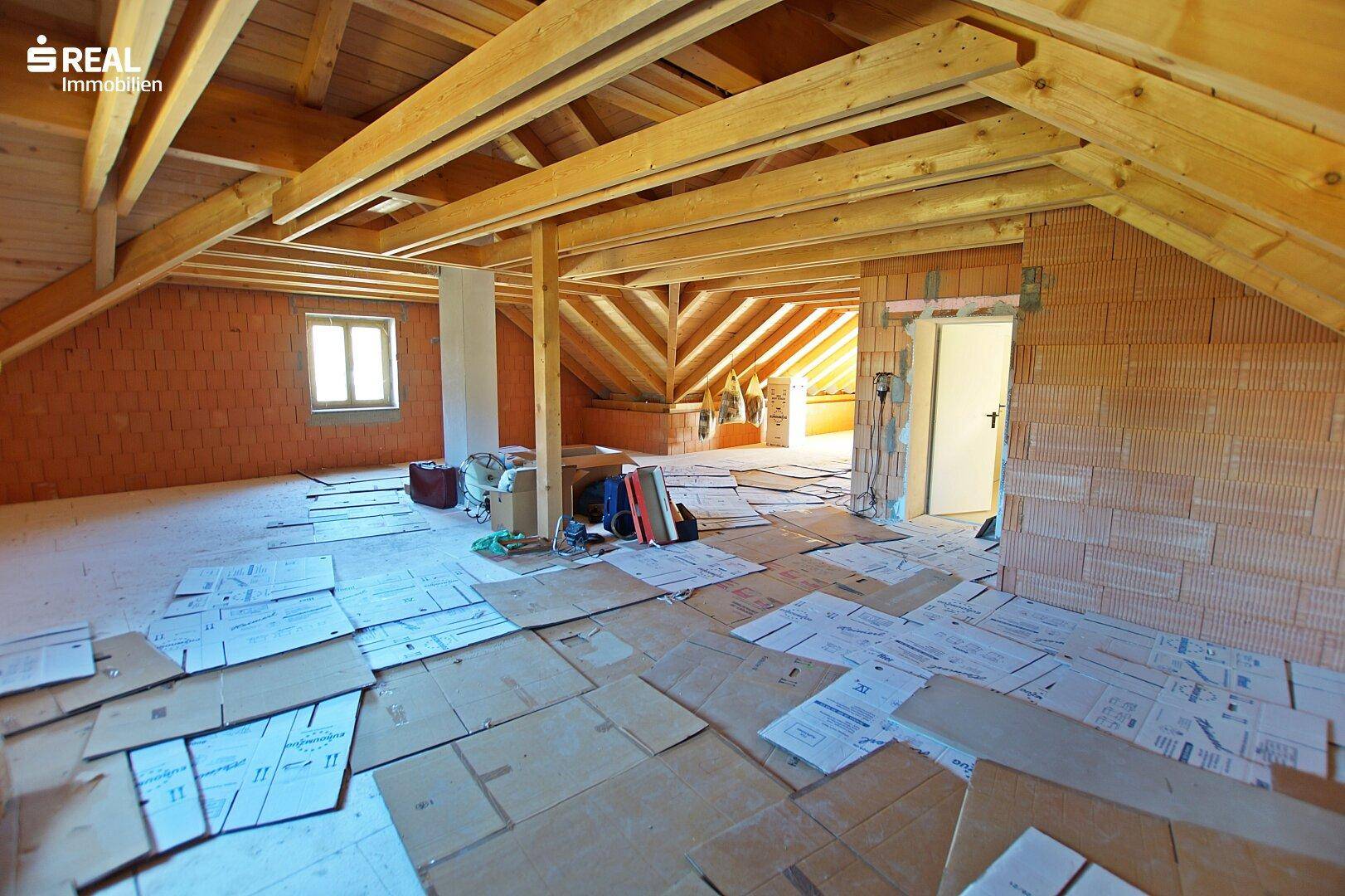 Unausgebauter Dachboden mit sichtbaren Holzbalken und Fenstern.
