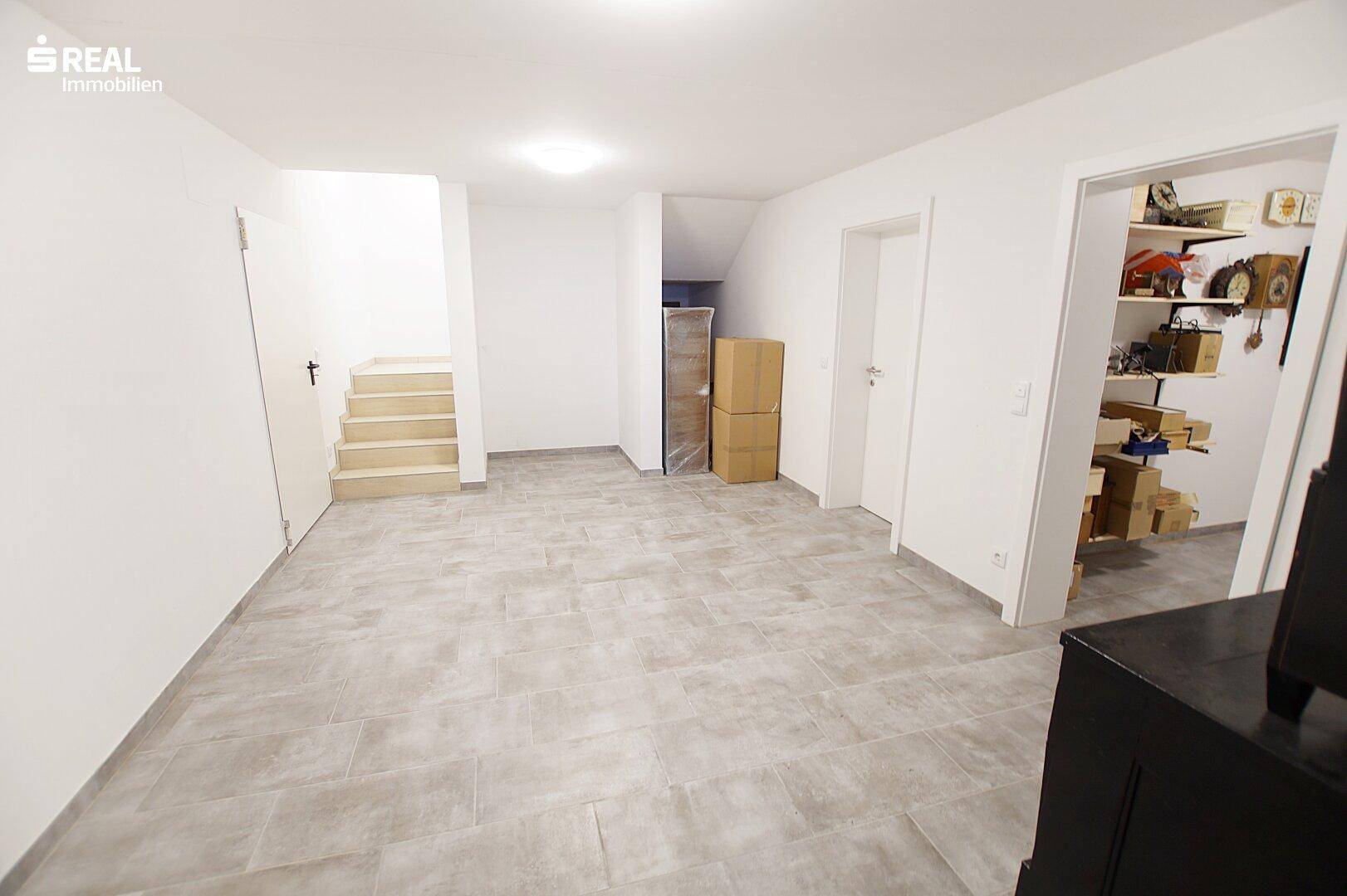 Ausgebauter Kellerraum mit Fliesenboden und Zugang zu weiteren Räumen.