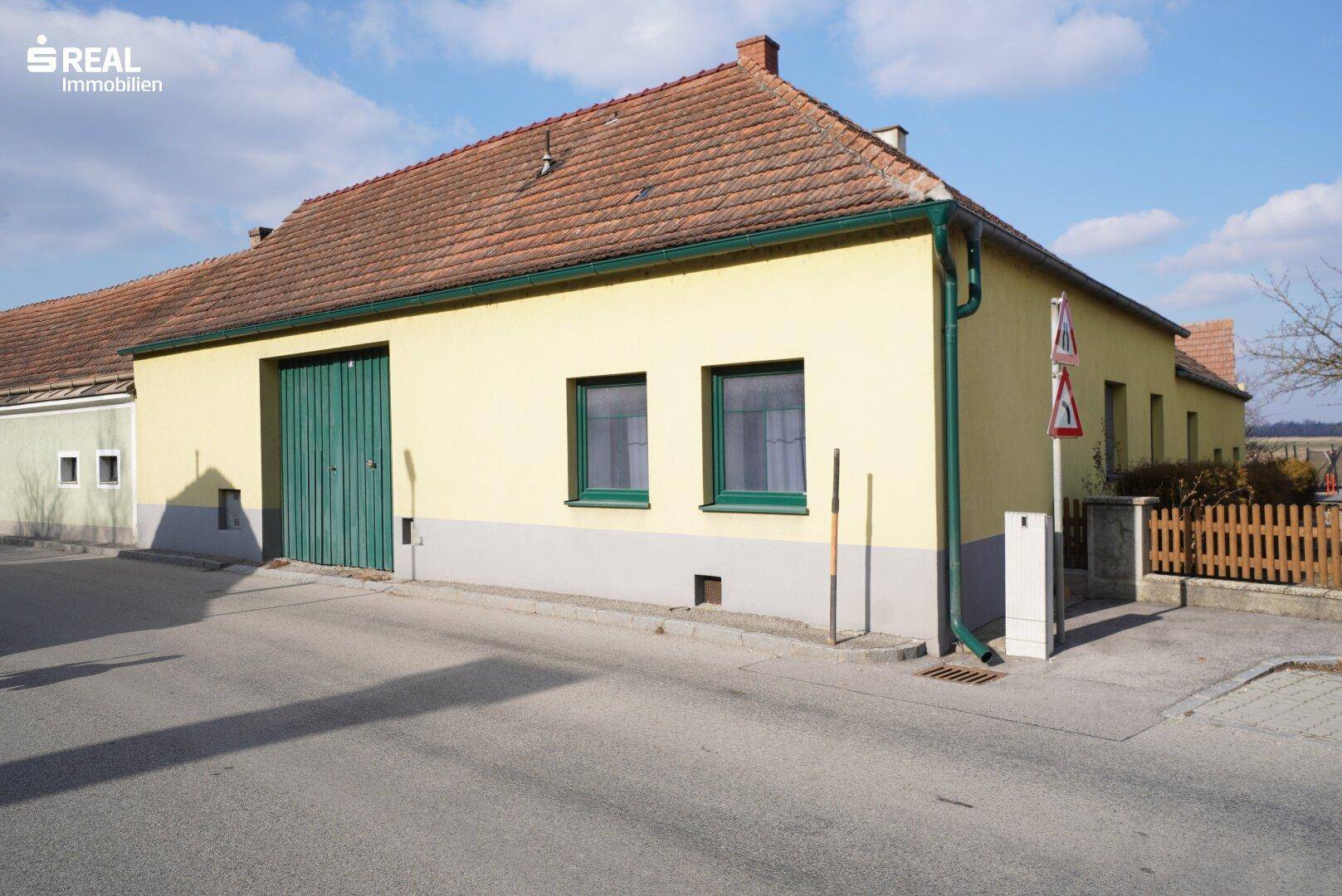 Ansicht des Hauses von der Straße mit gelber Fassade und grünen Garagentoren.