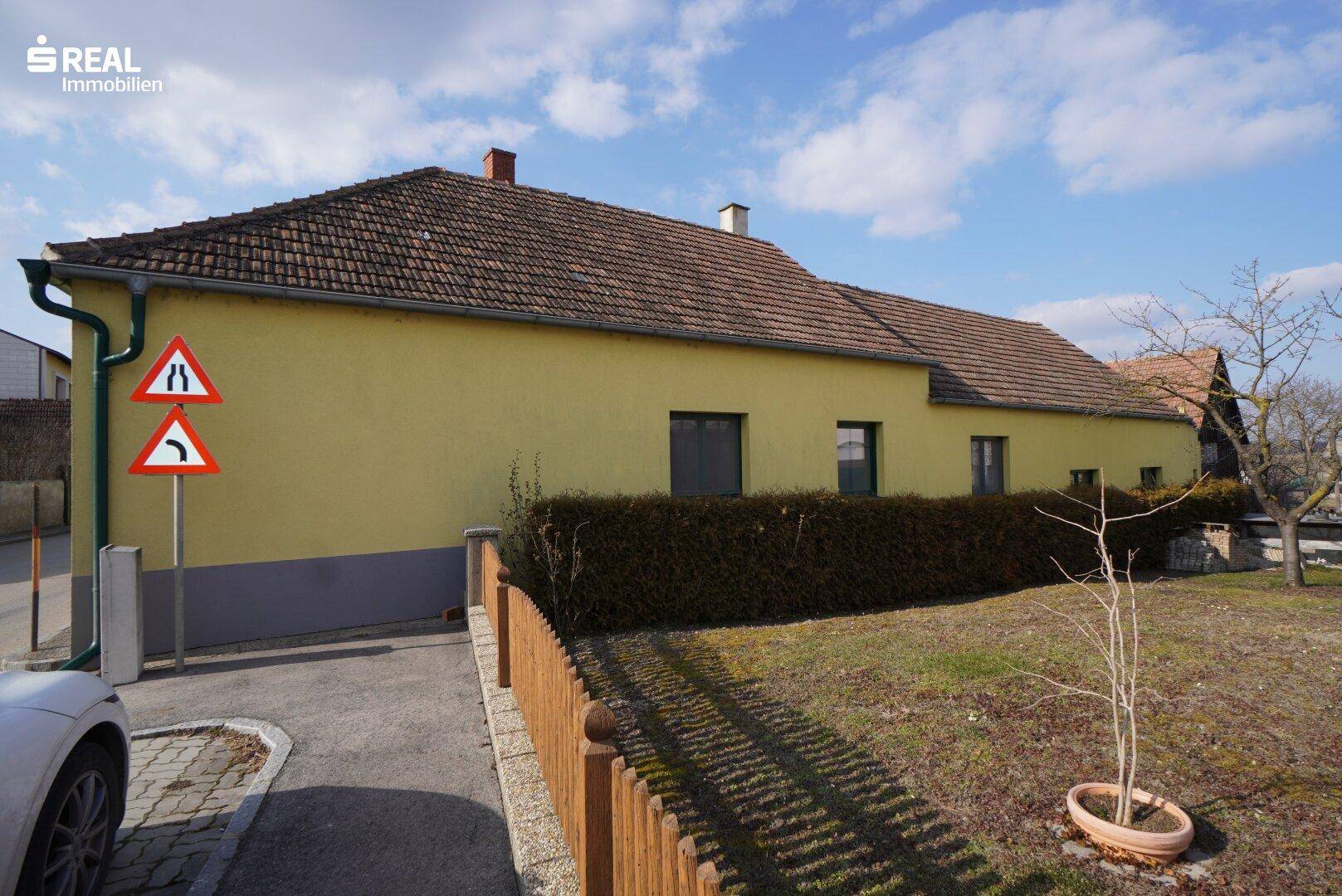 Seitenansicht des Hauses mit gelber Fassade, Ziegeldach und gepflegter Hecke.