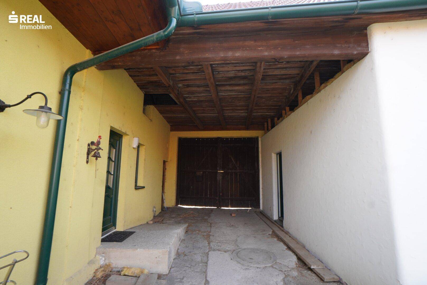 Überdachter Durchgangsbereich mit Holzbalkendecke und Zugang zu einem Nebengebäude.