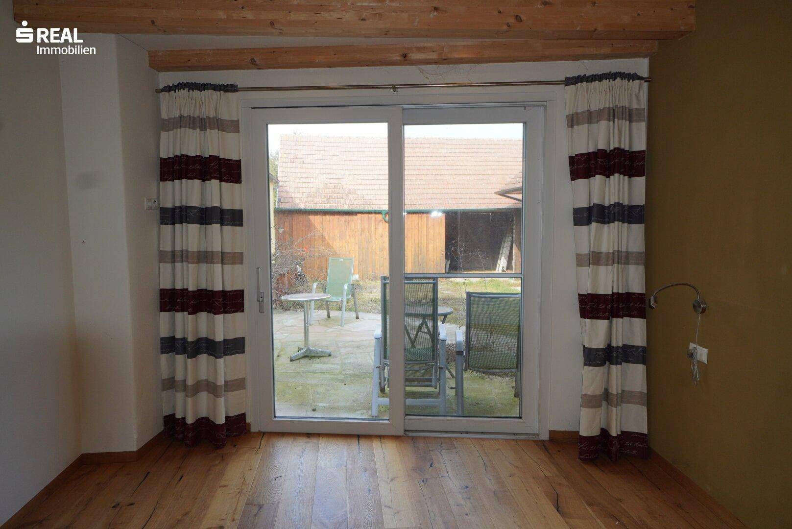 Zimmer mit Holzboden und großer Schiebetür, die zu einem Außenbereich führt.