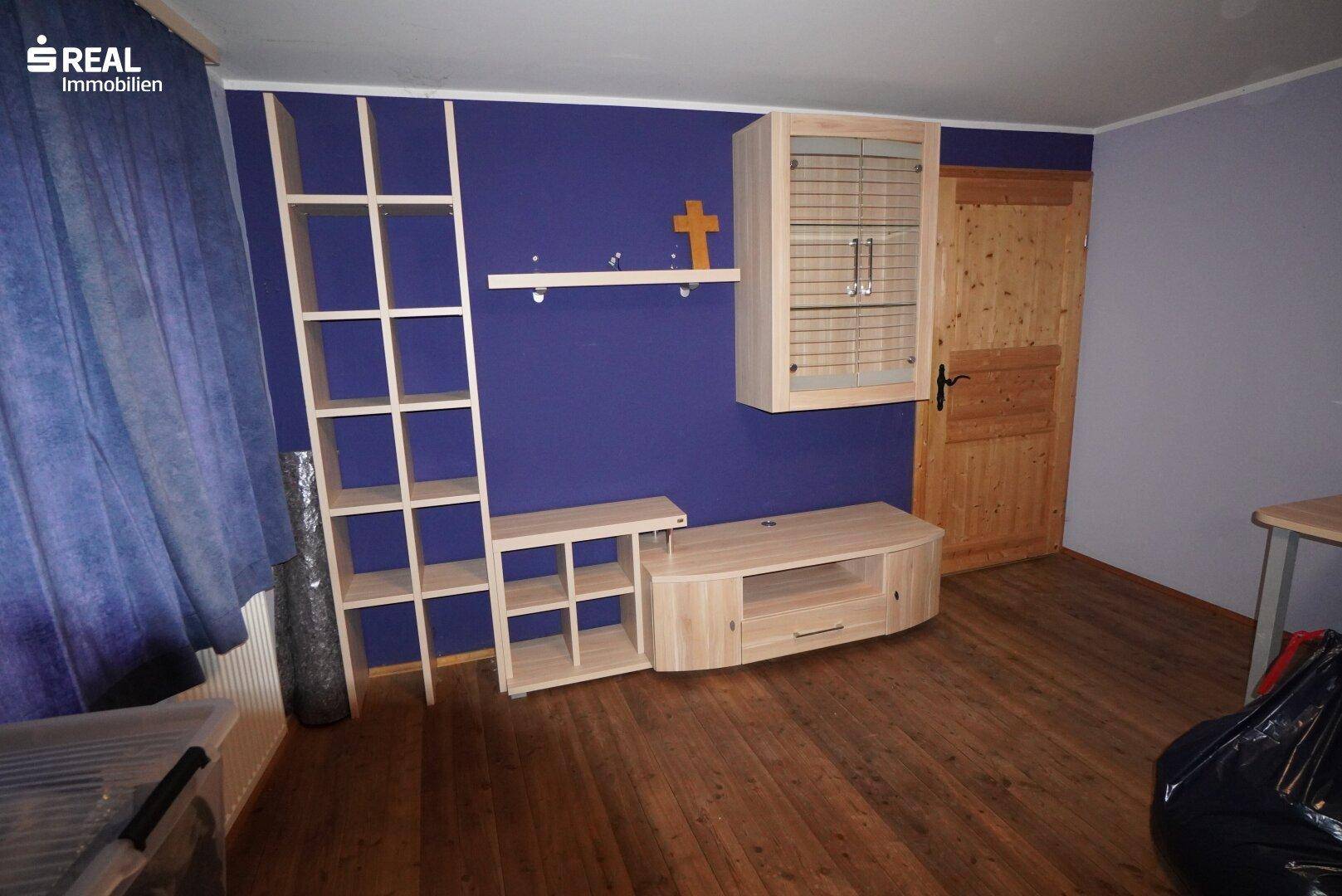 Zimmer mit Holzboden, blauer Wand und hellen Holzregalen.
