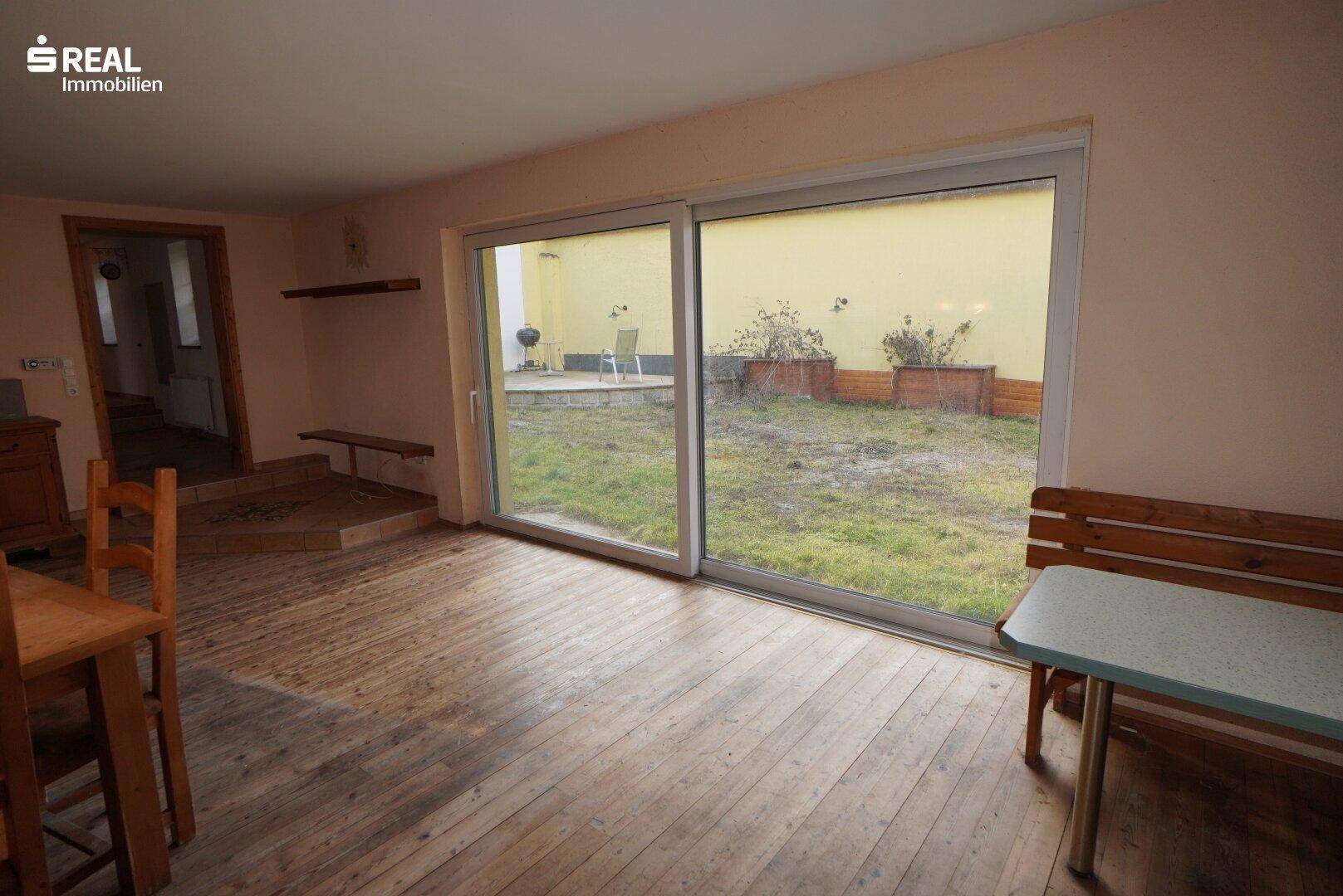 Wohnbereich mit Holzboden und großer Schiebetür zum Garten oder Innenhof.