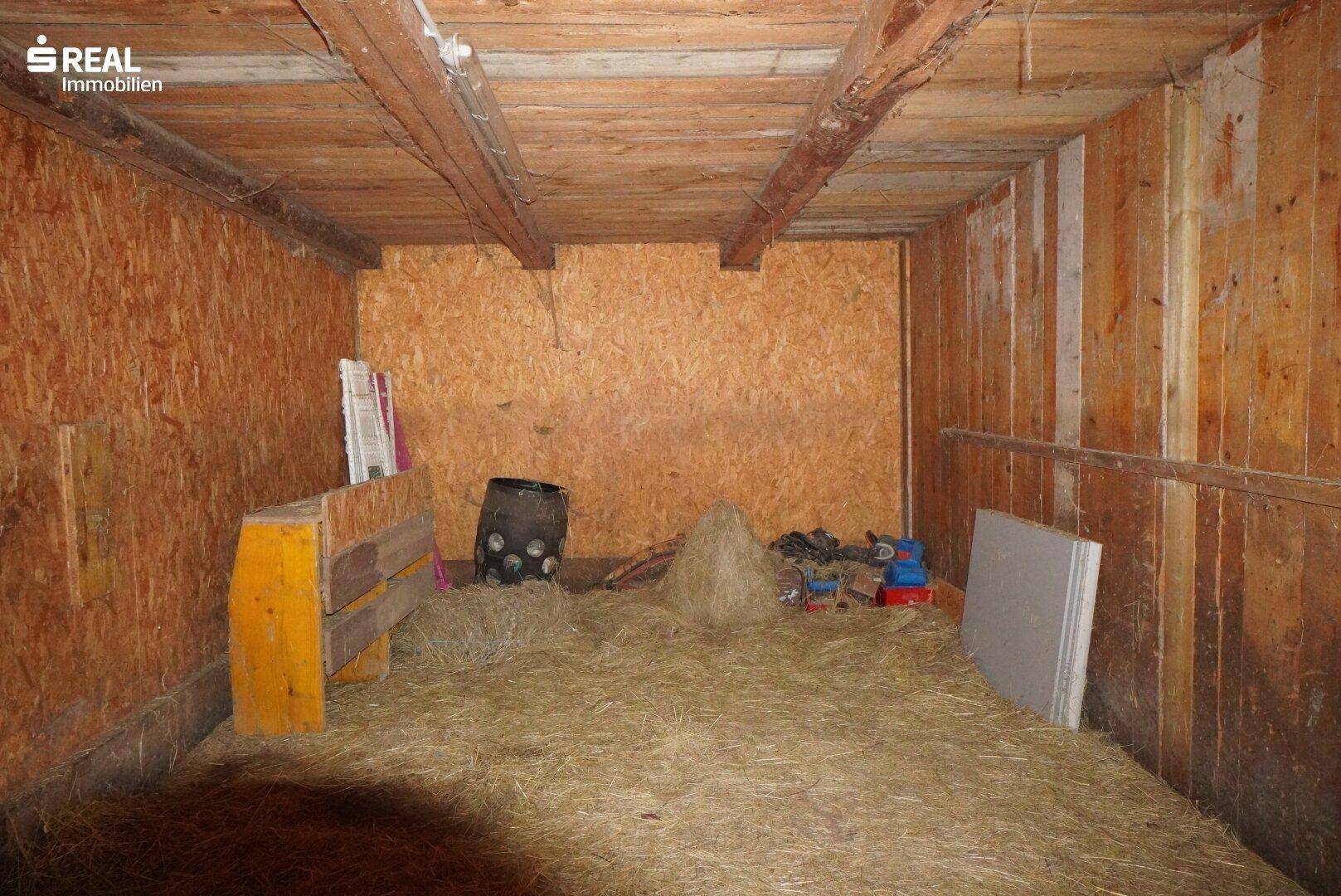 Innenansicht einer Scheune mit Holzwänden und Heu auf dem Boden.