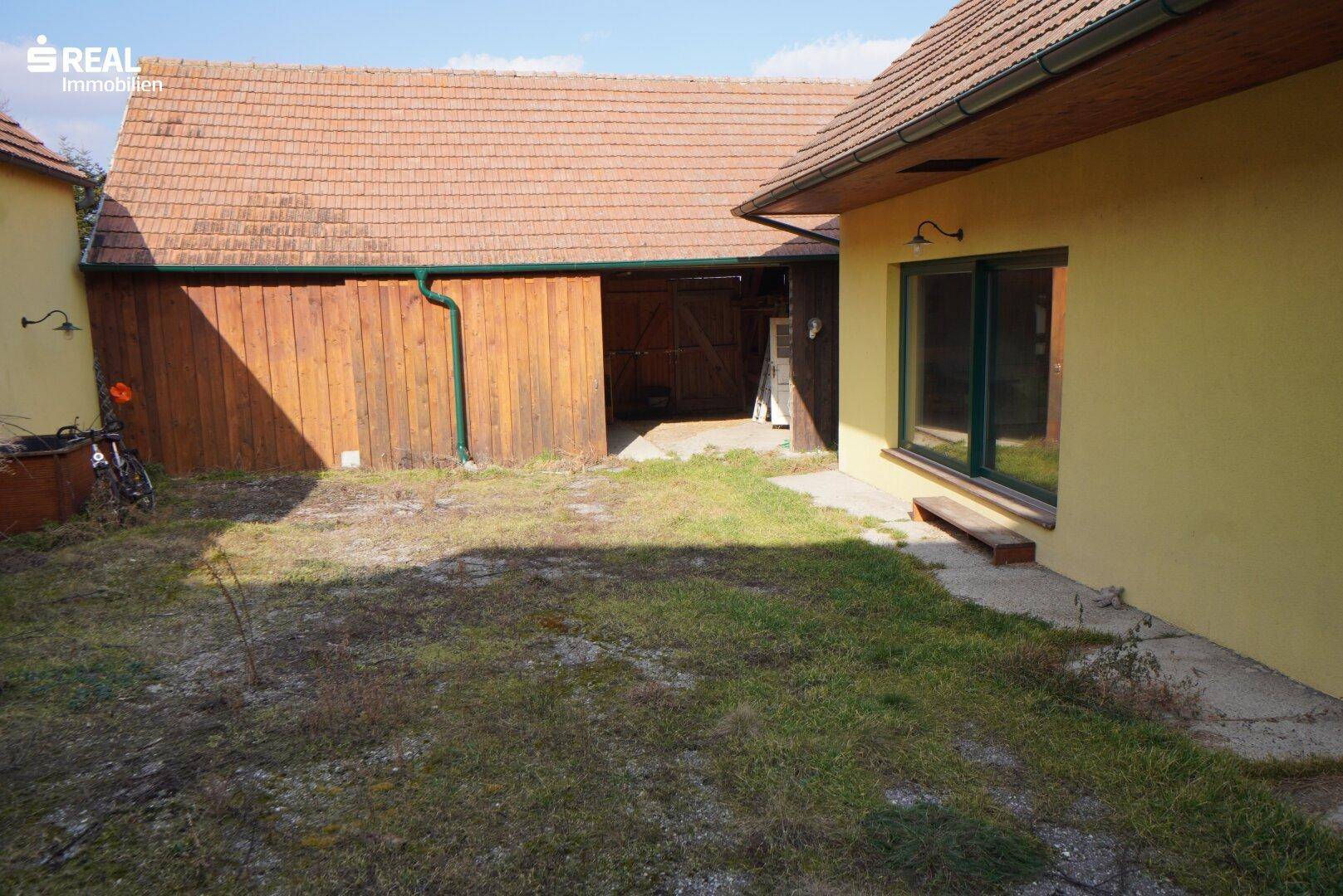 Gartenbereich mit Rasenfläche und einem Holzschuppen im Hintergrund.
