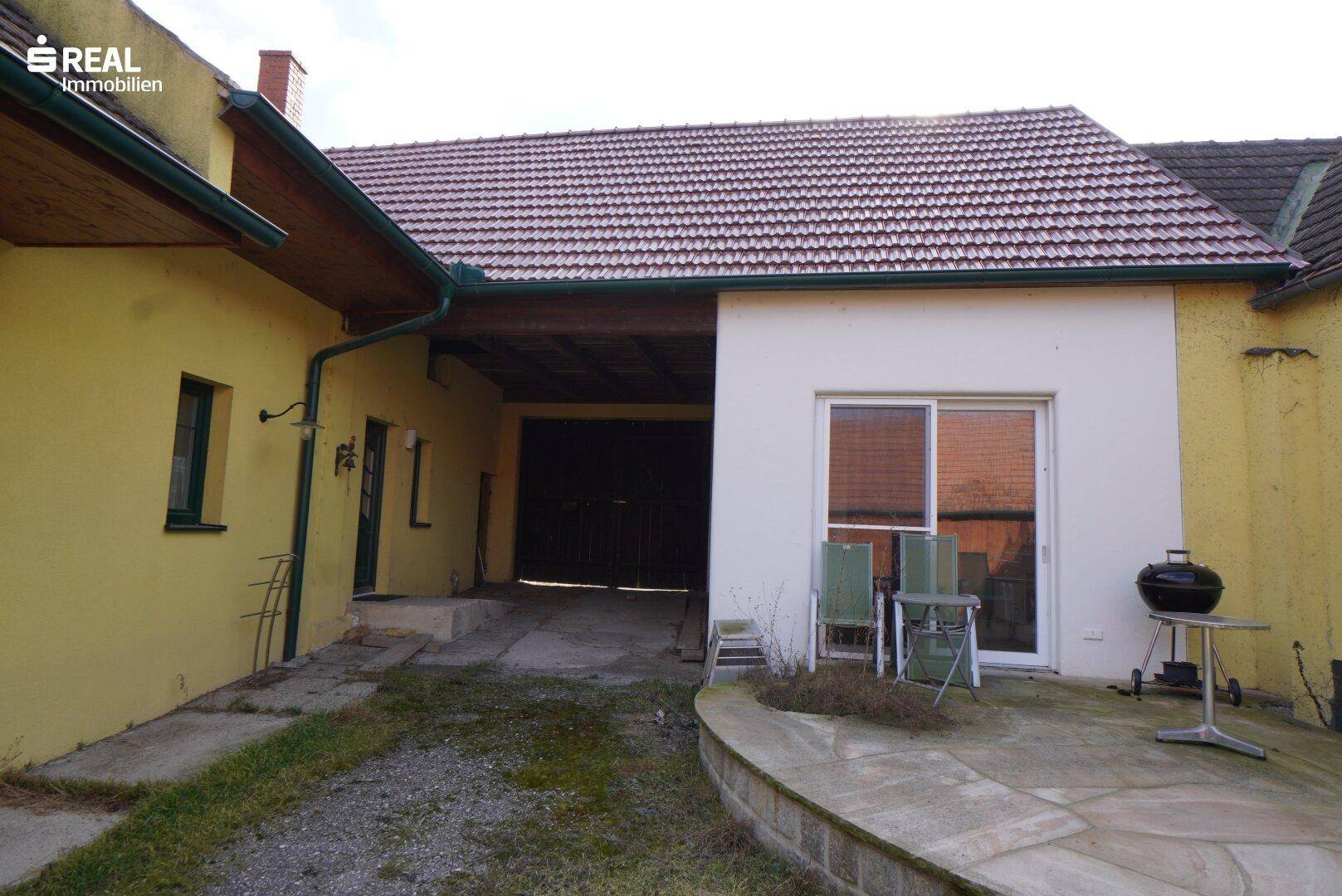 Kleine gepflasterte Terrasse mit Grill und Sitzgelegenheiten neben dem Haus.