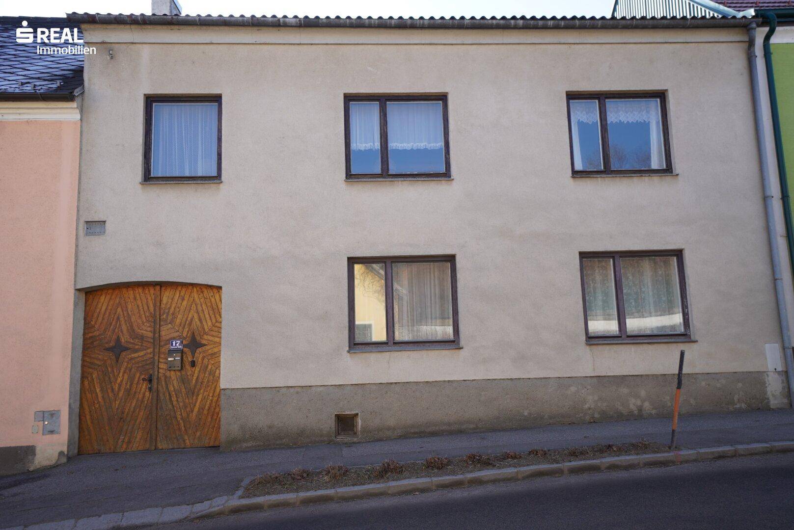 Fassade eines älteren Wohnhauses mit mehreren Fenstern und einem großen Holztor.
