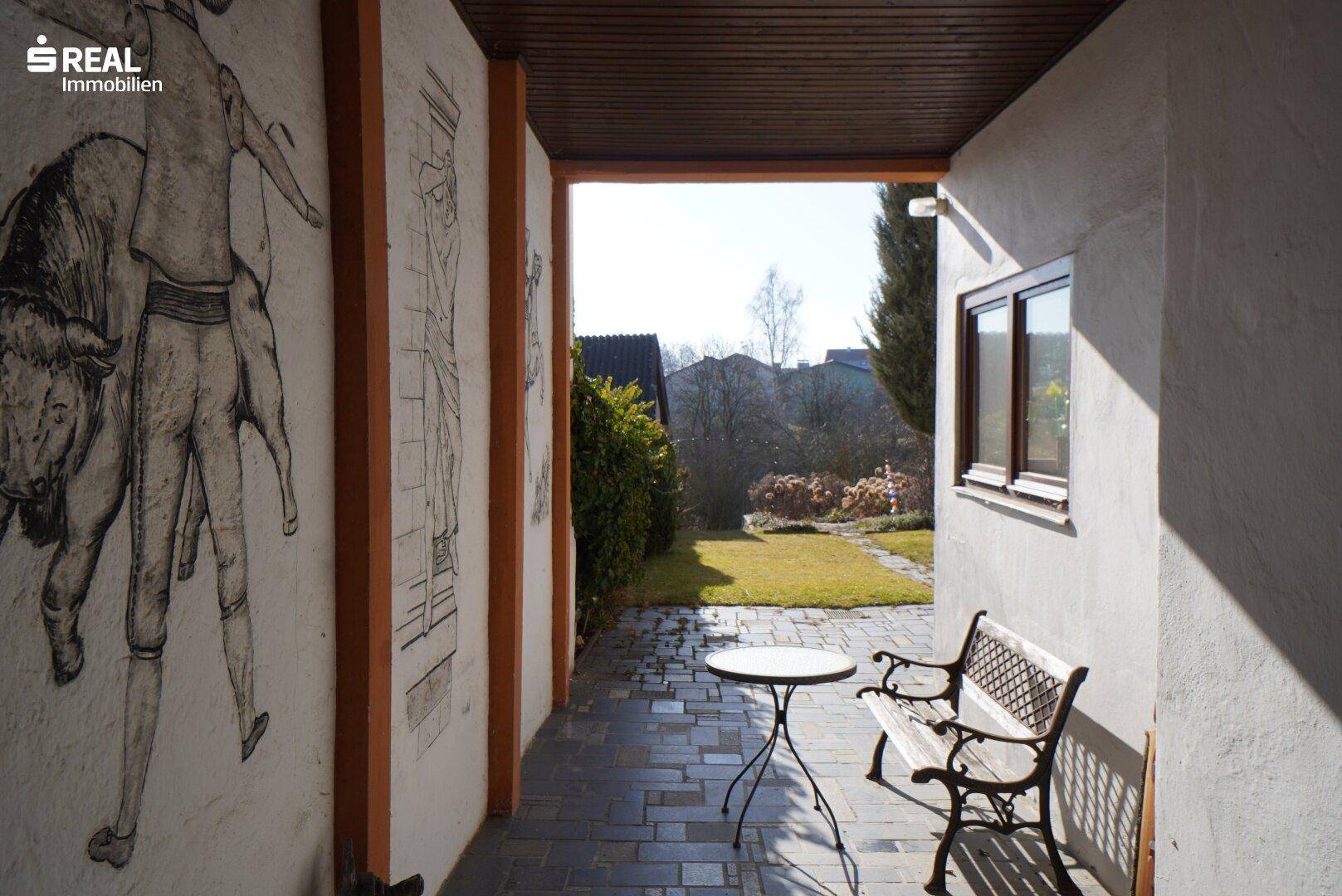 Überdachter Außenbereich mit Sitzgelegenheiten und Blick auf den Garten.