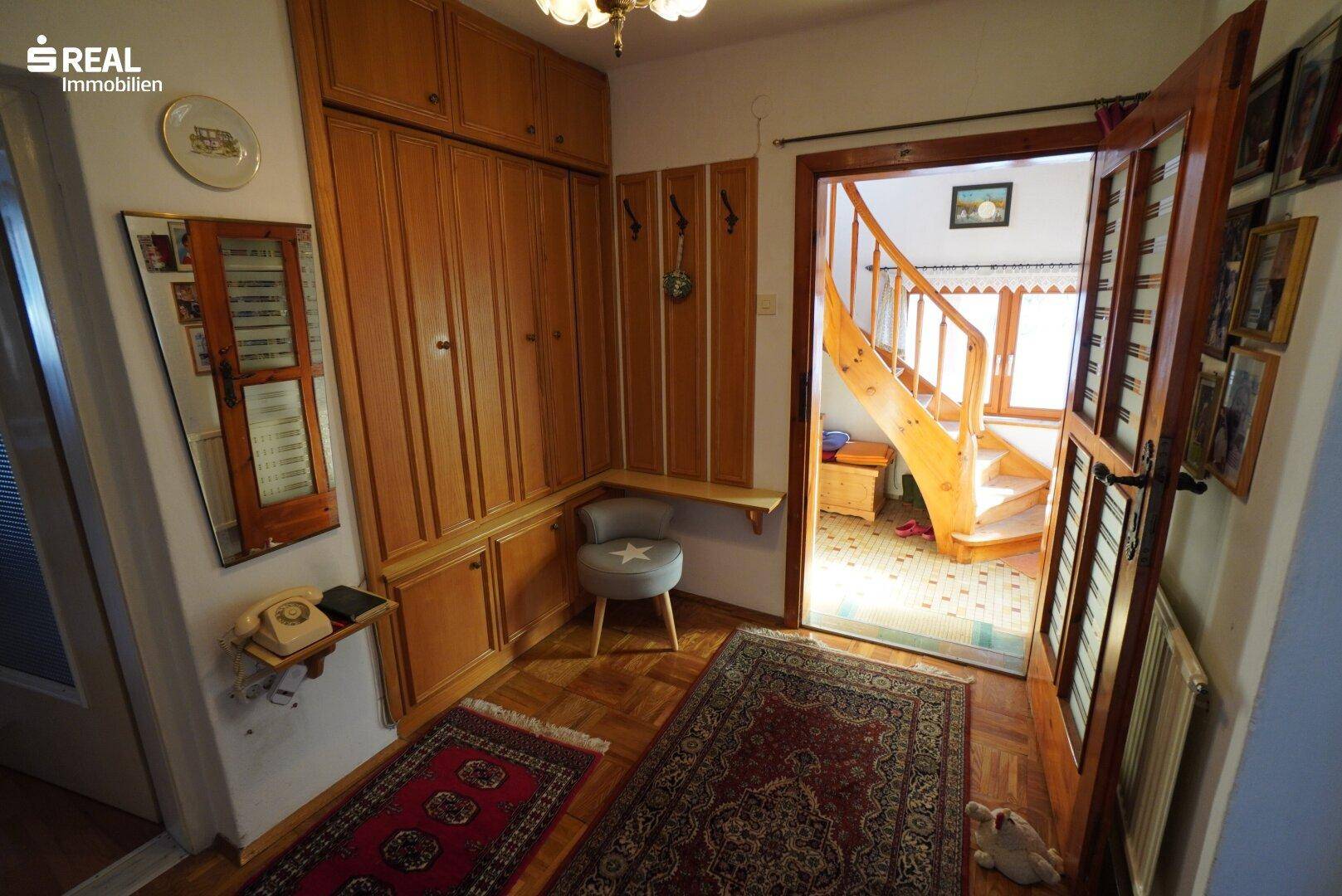 Eingangsbereich mit Holzparkett, Einbauschränken und einer Holztreppe zum Obergeschoss.