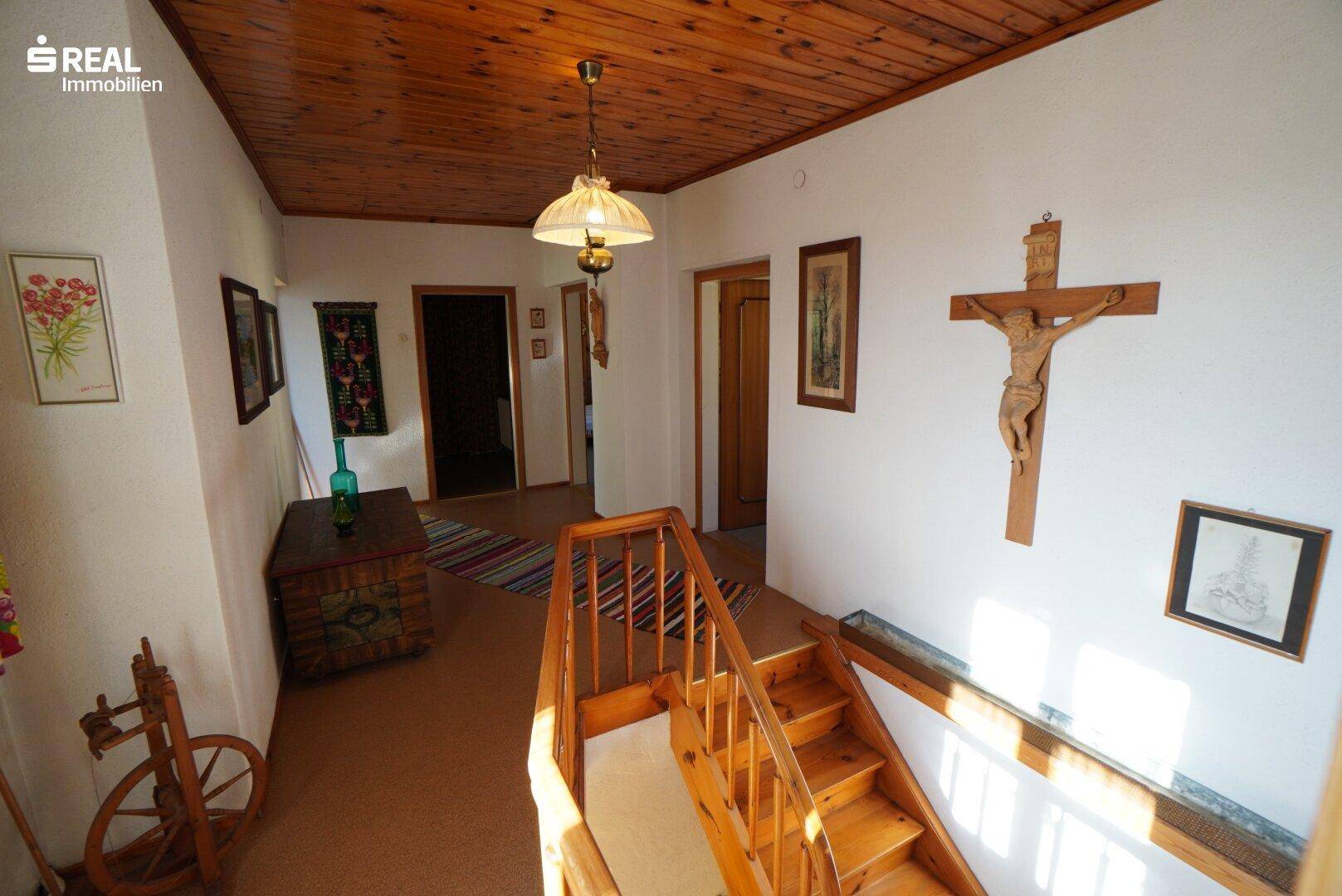 Heller Flur im Obergeschoss mit Holztreppe, Holzbalkendecke und Teppichboden.